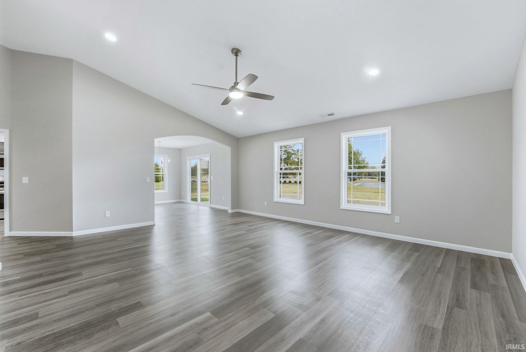 Unfurnished room featuring arched walkways, a ceiling fan, light wood finished floors, healthy amount of natural light, and vaulted ceiling
