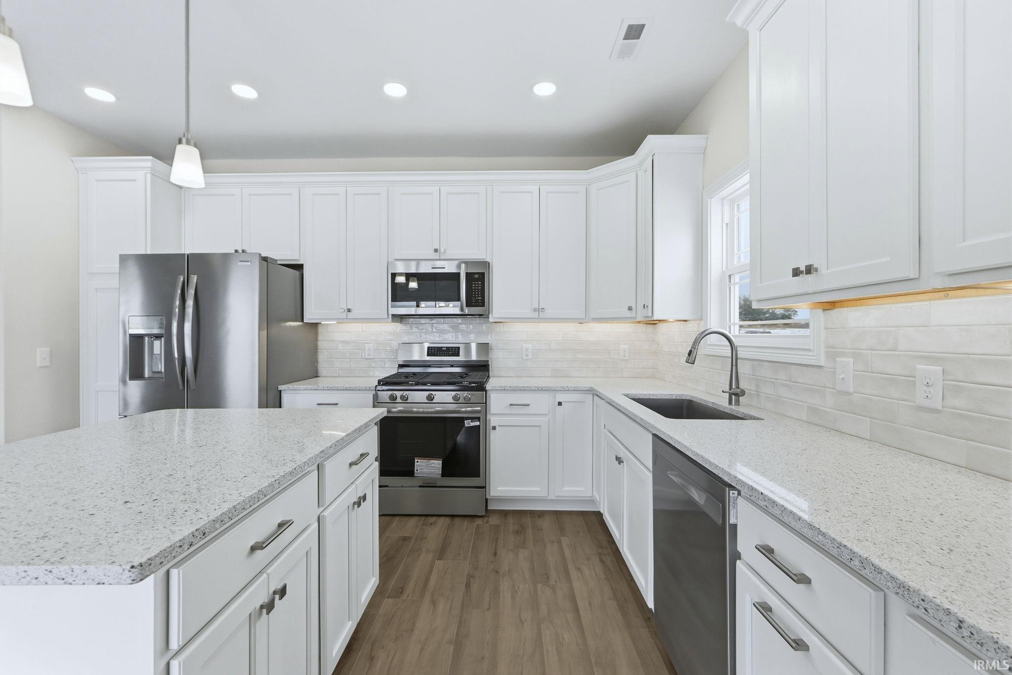 Kitchen featuring stainless steel appliances, white cabinetry, decorative light fixtures, and dark wood-style floors