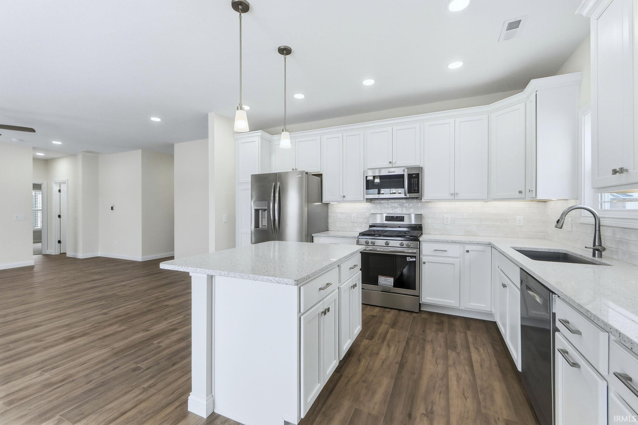 Kitchen with hanging light fixtures, stainless steel appliances, a kitchen island, white cabinetry, and open floor plan