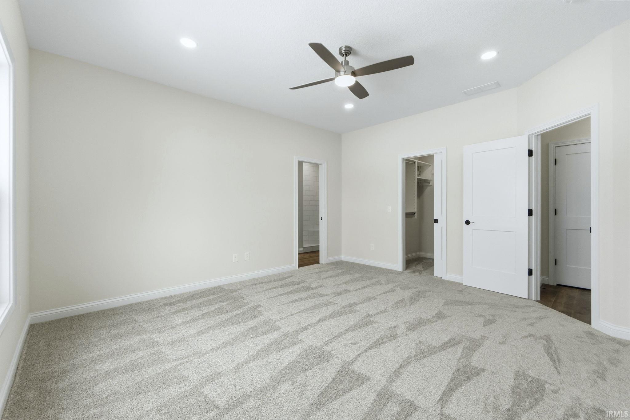 Unfurnished bedroom featuring light carpet, a spacious closet, ceiling fan, and recessed lighting