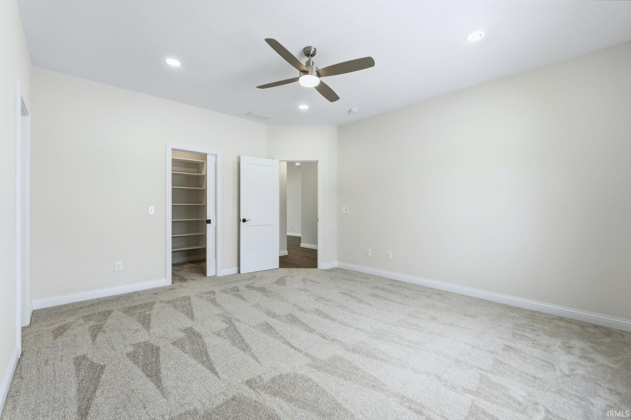 Unfurnished bedroom featuring a walk in closet, a ceiling fan, light carpet, and recessed lighting