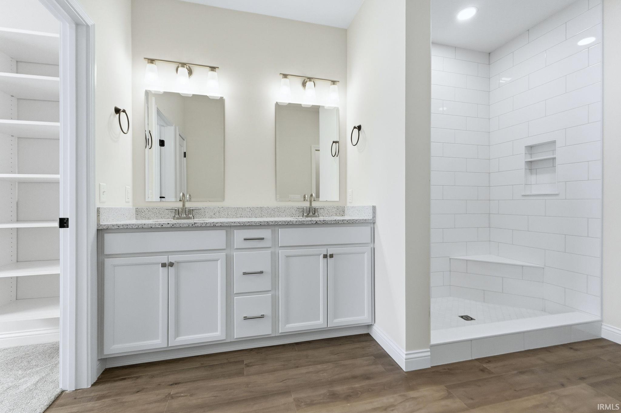 Full bath featuring double vanity, a tile shower, light wood finished floors, and a spacious closet
