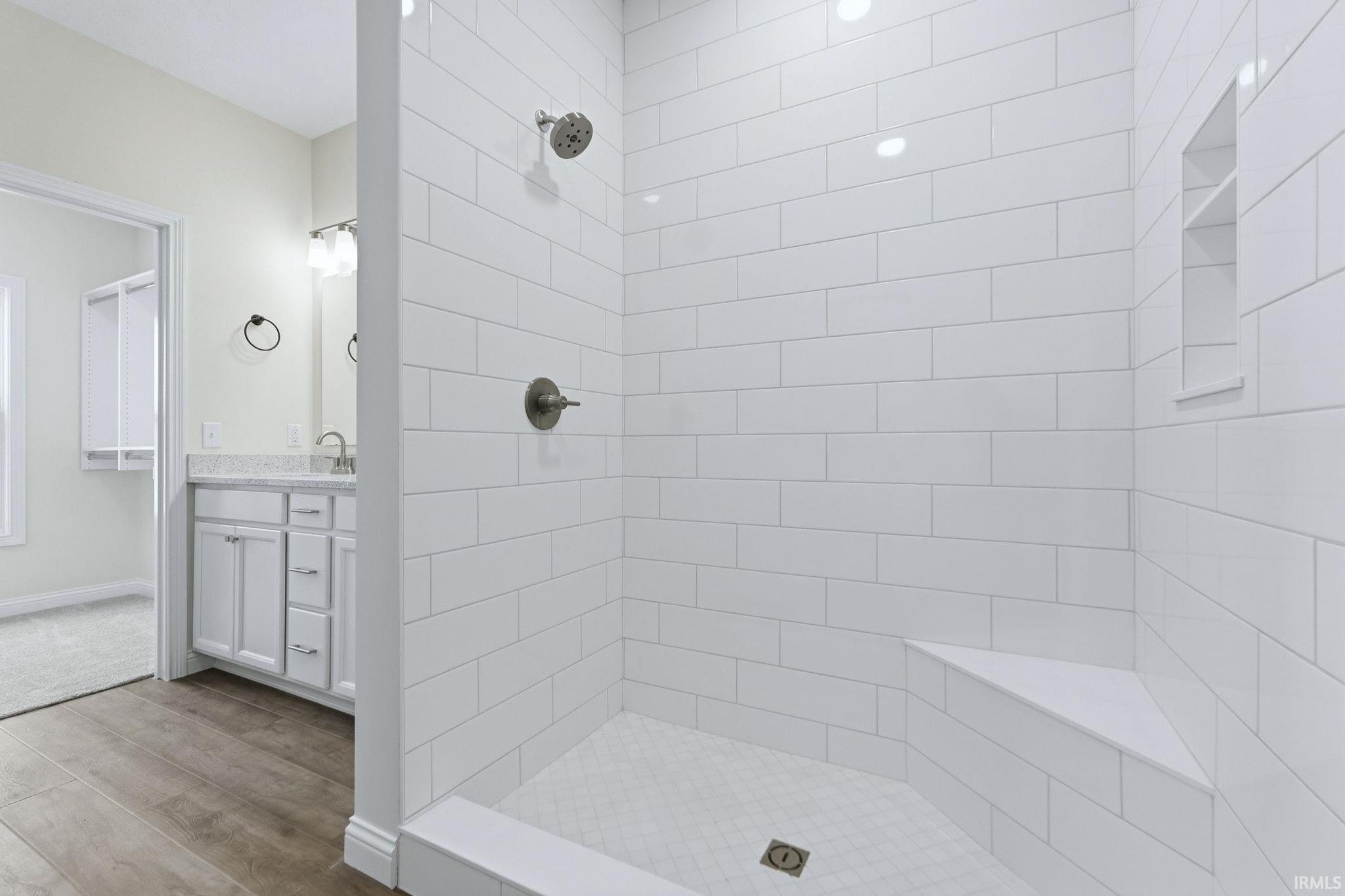 Full bathroom with light wood-type flooring, vanity, and tiled shower