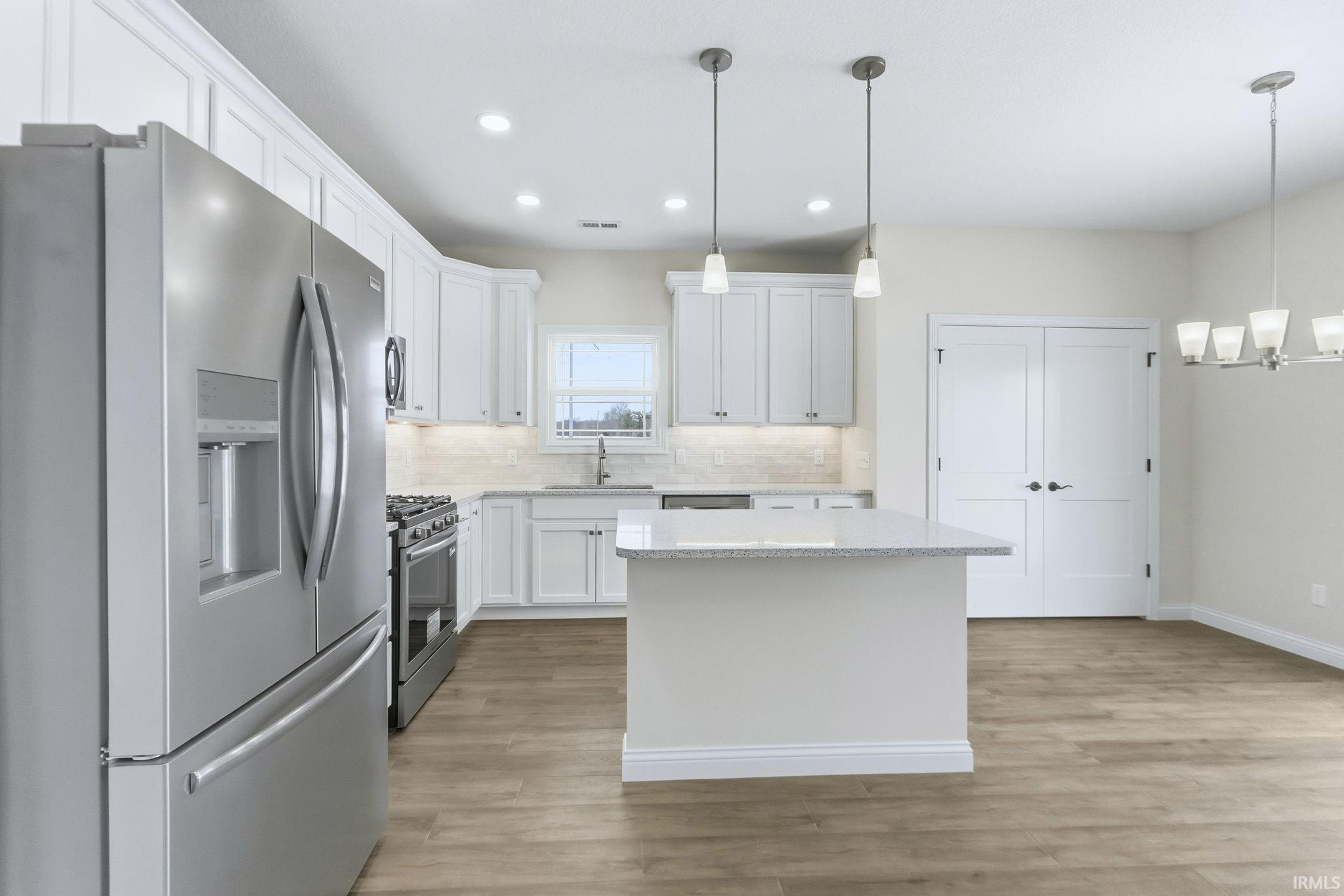 Kitchen featuring stainless steel appliances, white cabinets, decorative backsplash, a kitchen island, and light wood-style flooring