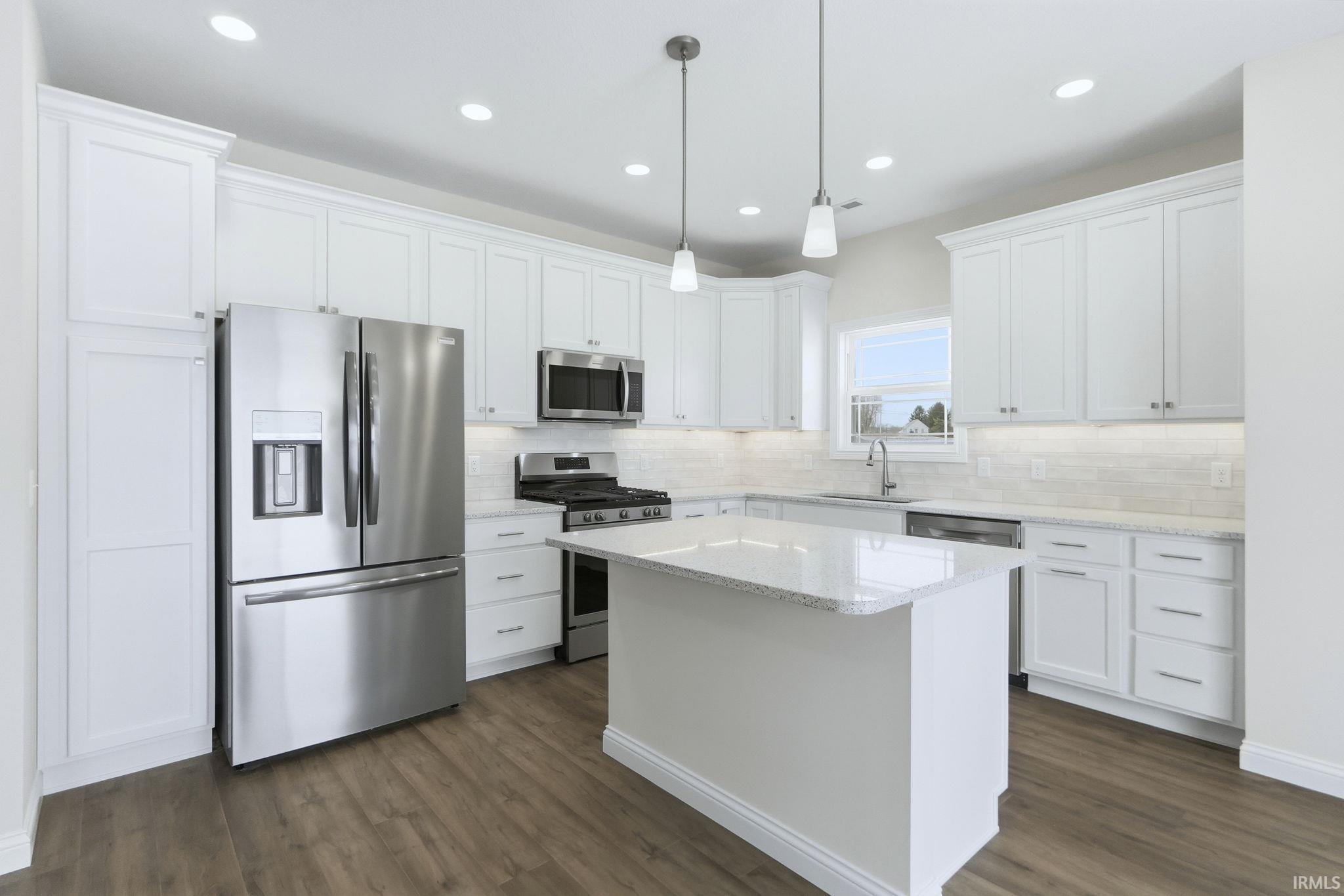 Kitchen featuring stainless steel appliances, white cabinets, decorative light fixtures, and light stone counters