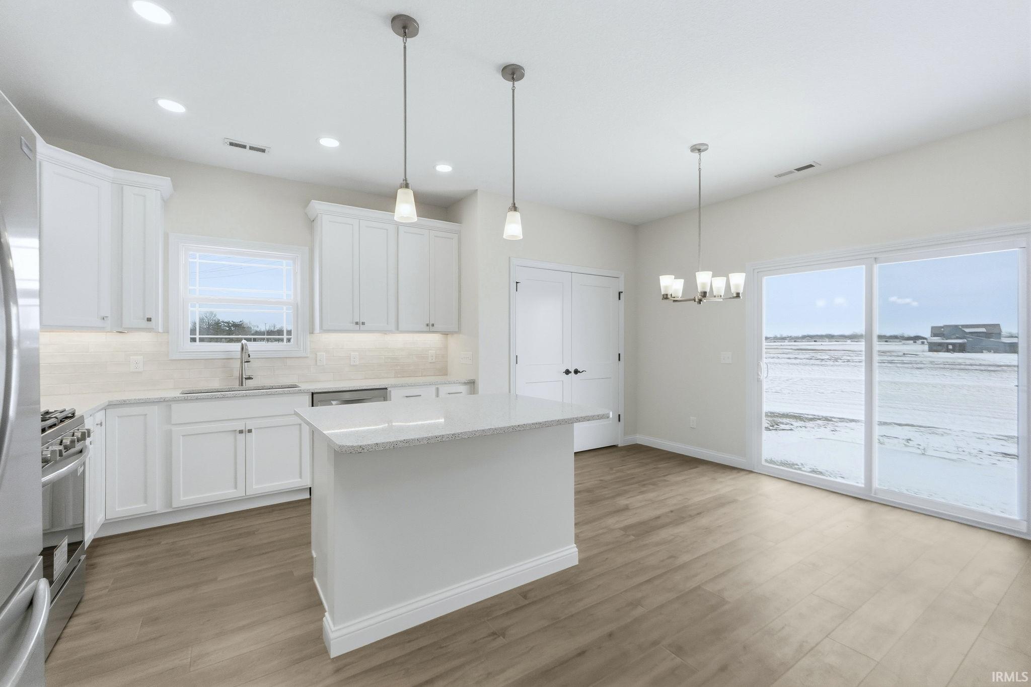 Kitchen with white cabinetry, hanging lights, light stone countertops, a kitchen island, and light wood-style flooring