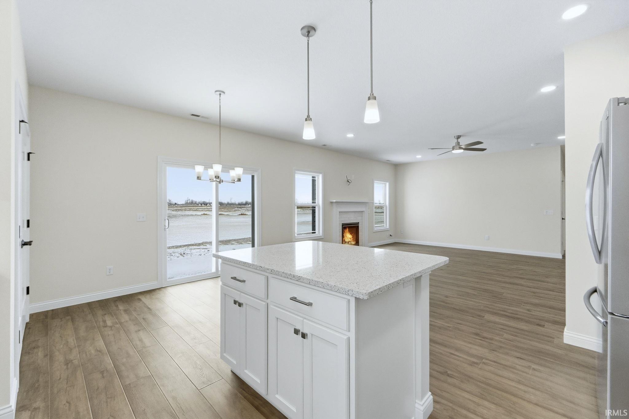 Kitchen with a lit fireplace, freestanding refrigerator, open floor plan, white cabinetry, and light stone counters