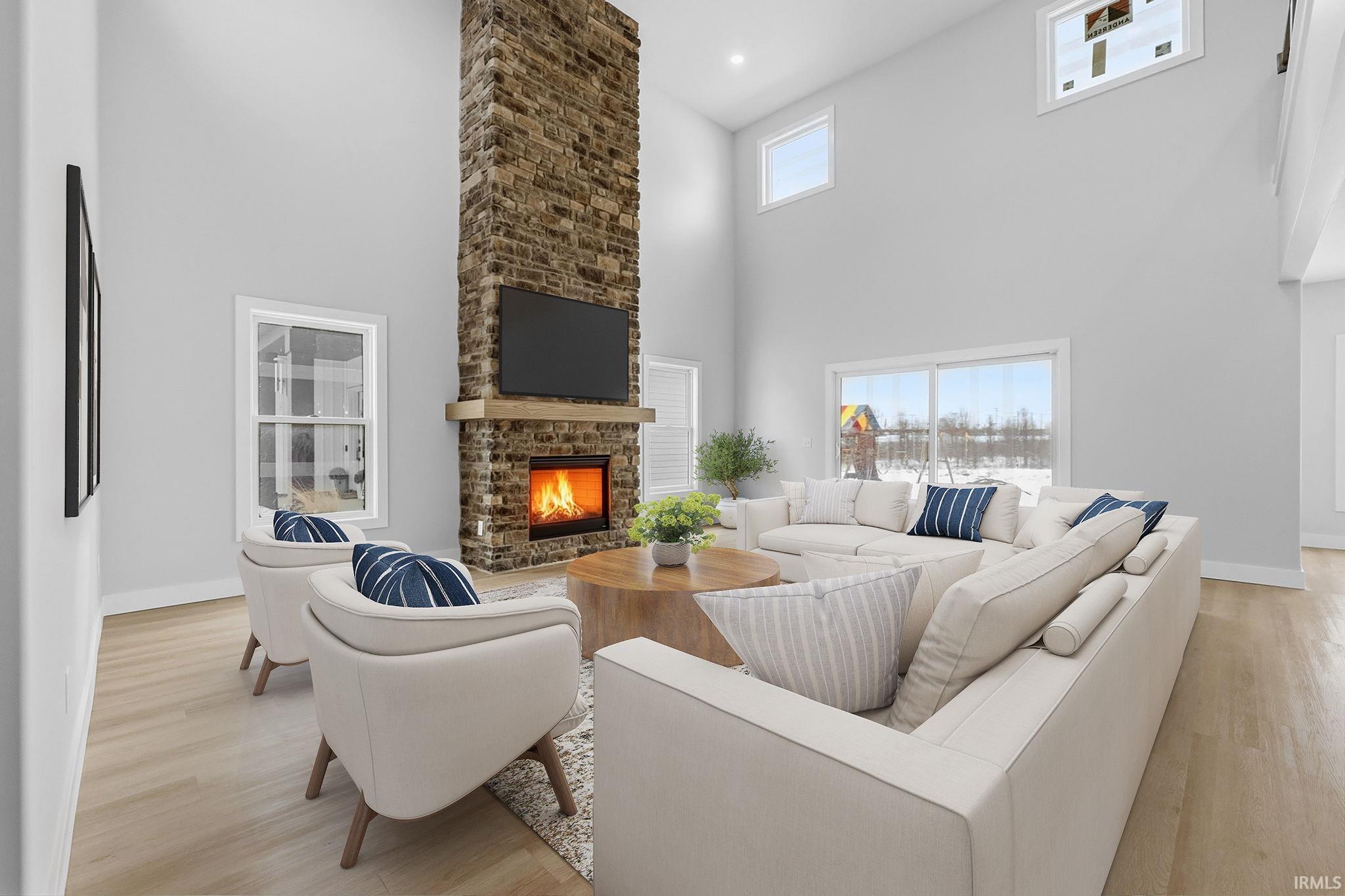 Living area featuring a high ceiling, a large fireplace, light wood-type flooring, and healthy amount of natural light