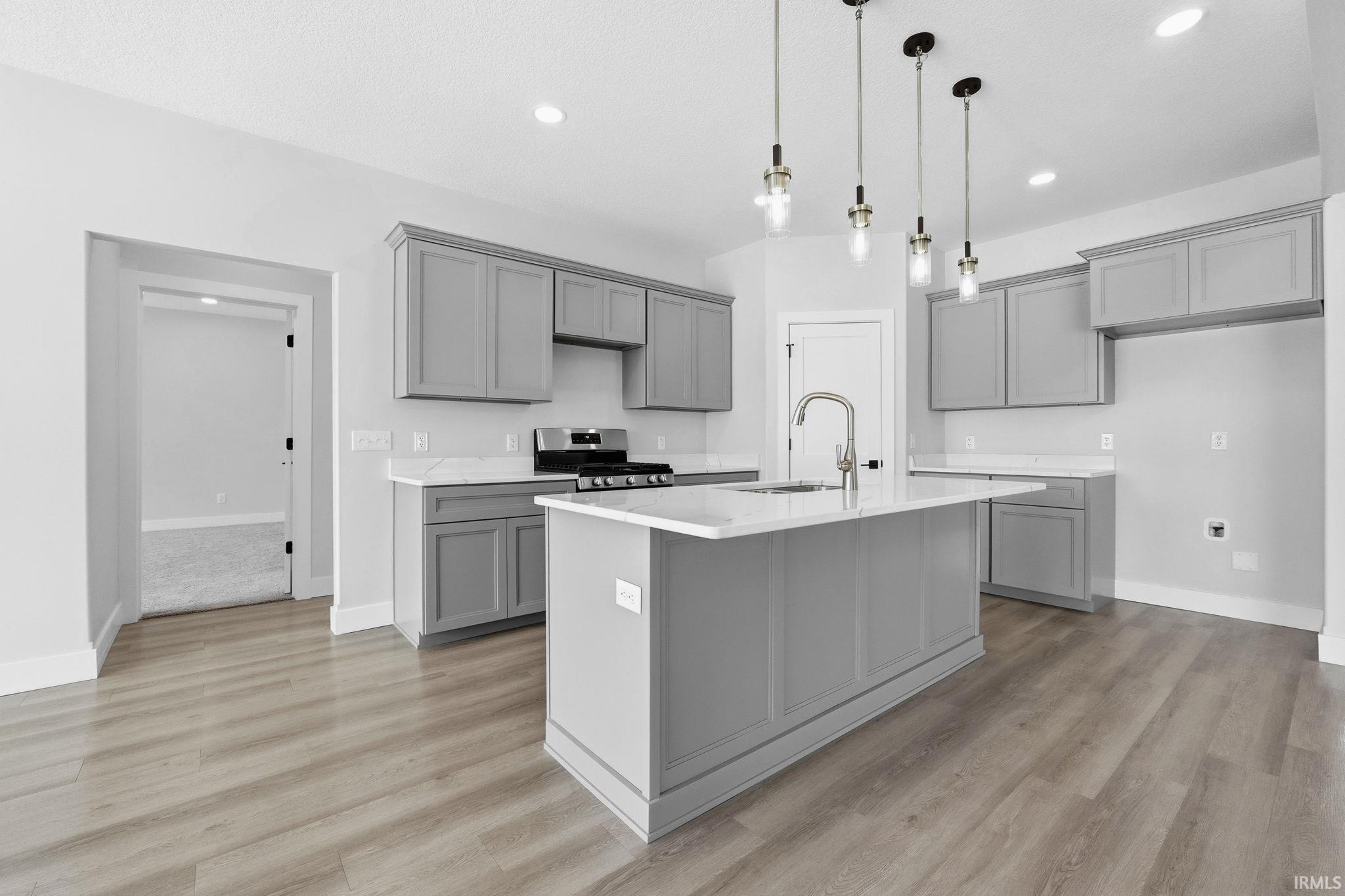 Kitchen with gray cabinetry, stainless steel gas range oven, hanging light fixtures, and a center island with sink