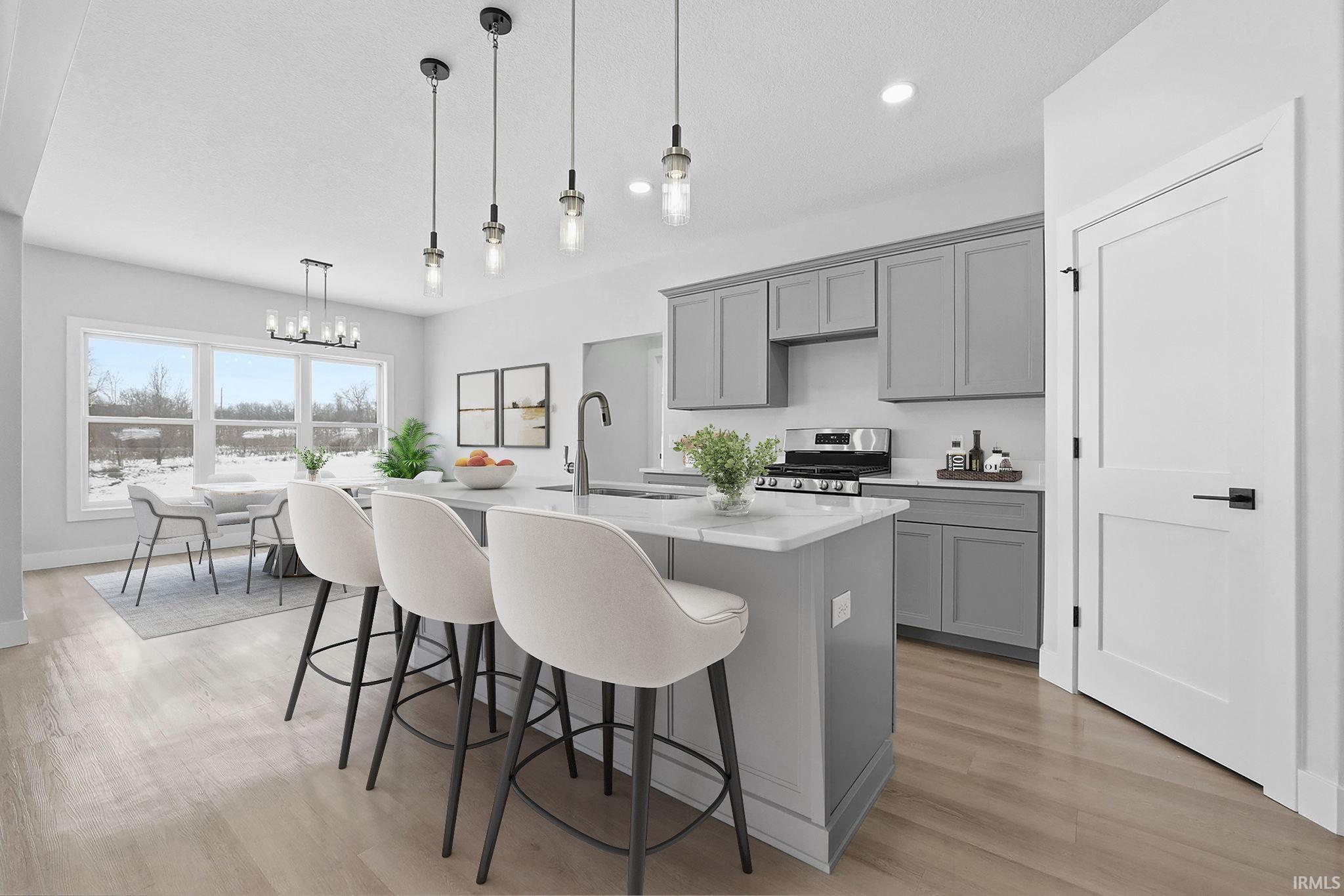 Kitchen with gray cabinetry, a center island with sink, a breakfast bar area, stainless steel range with gas stovetop, and light stone counters