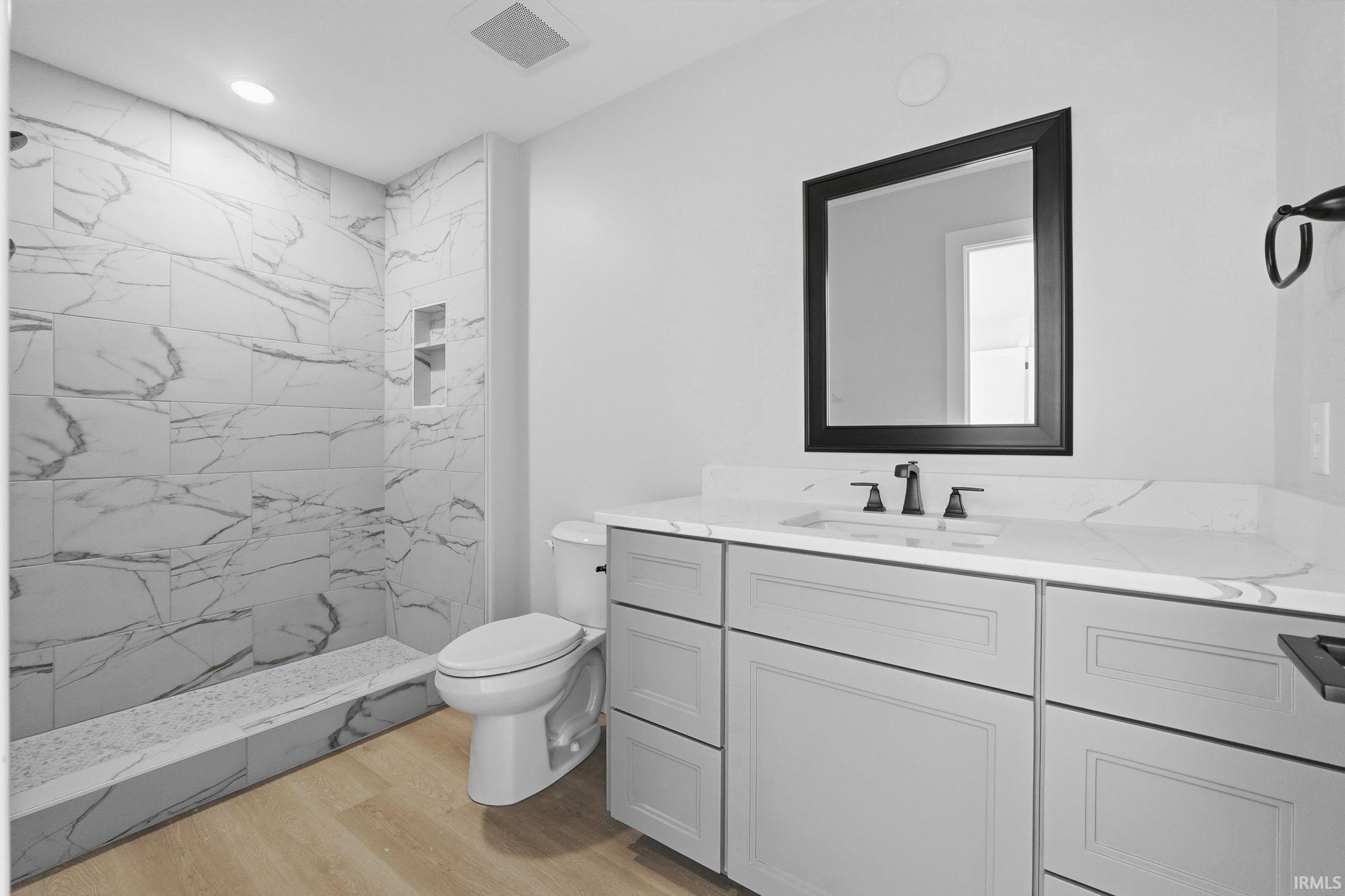 Full bath featuring a marble finish shower, vanity, light wood-style floors, and recessed lighting