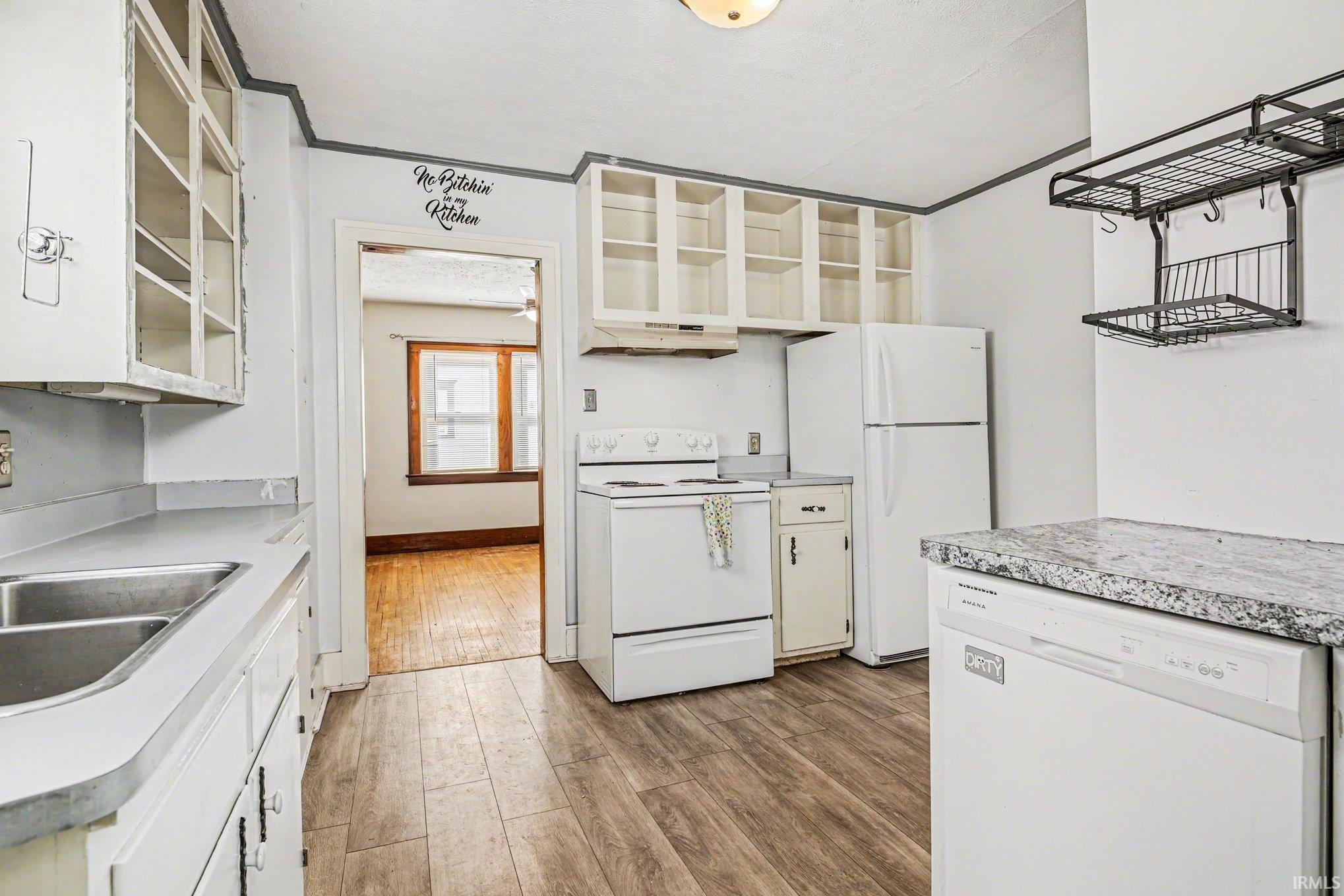 Kitchen with white appliances, white cabinets, light countertops, light wood-type flooring, and glass insert cabinets