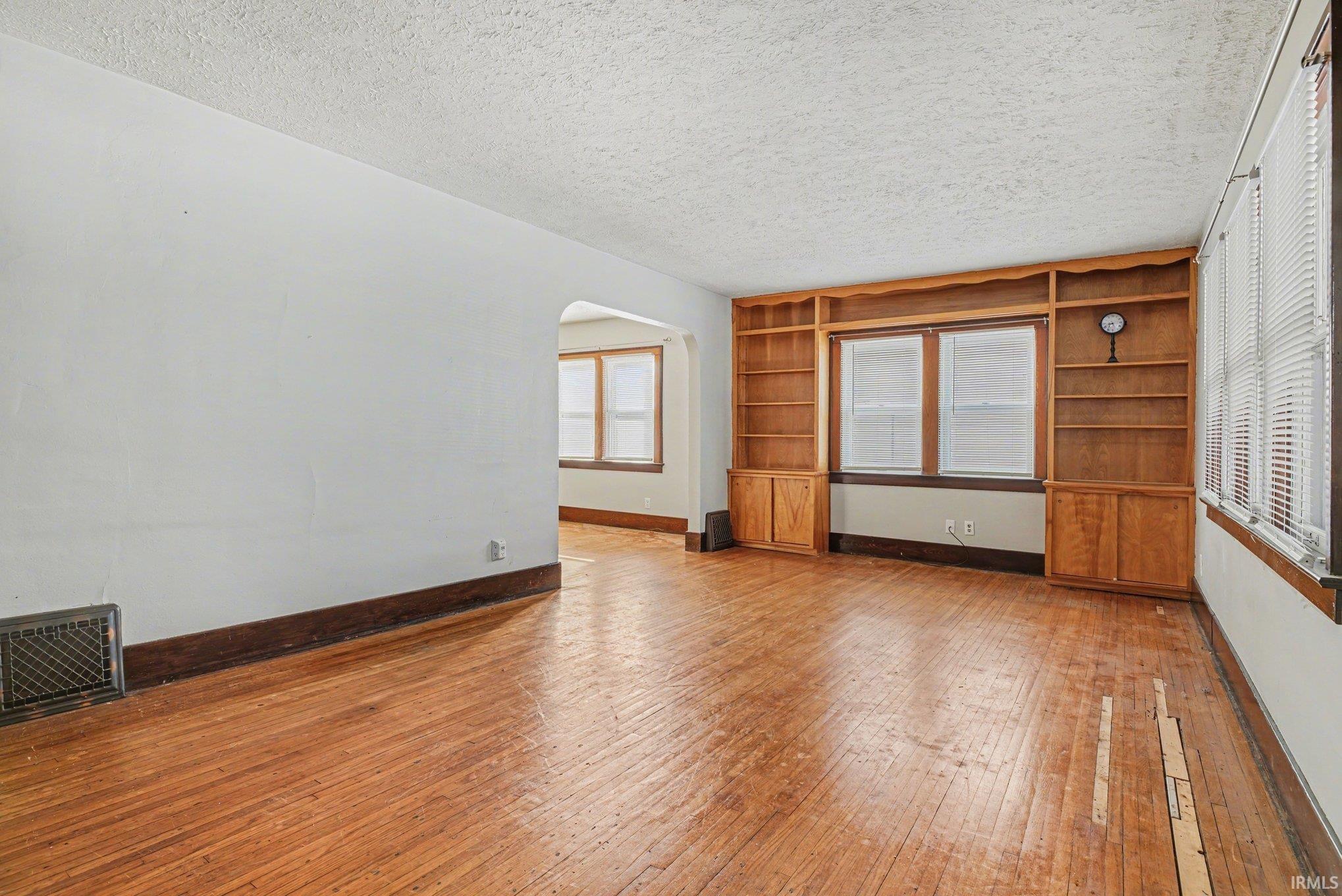 Unfurnished living room with arched walkways, light wood-type flooring, and a textured ceiling