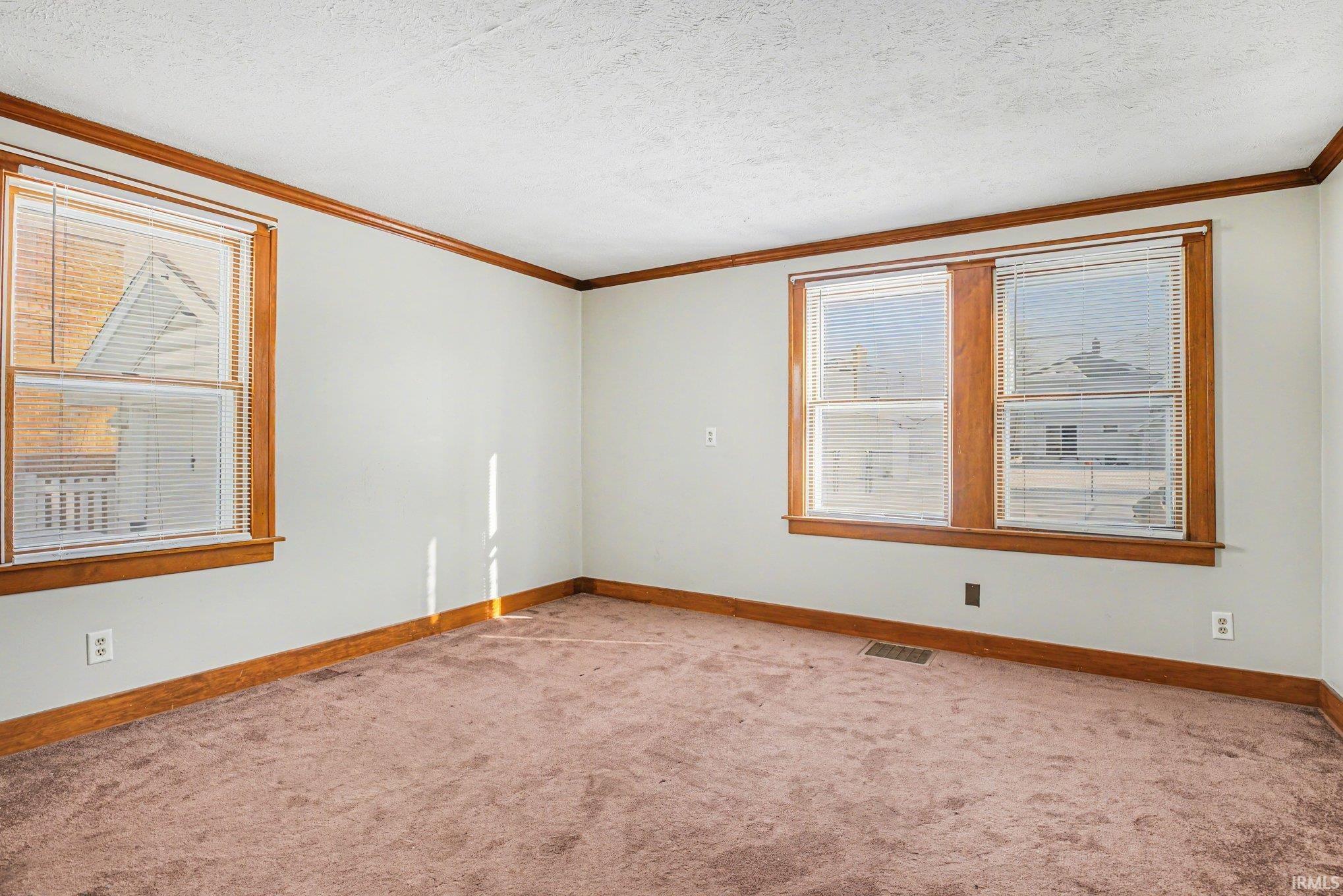 Carpeted empty room featuring ornamental molding and a textured ceiling