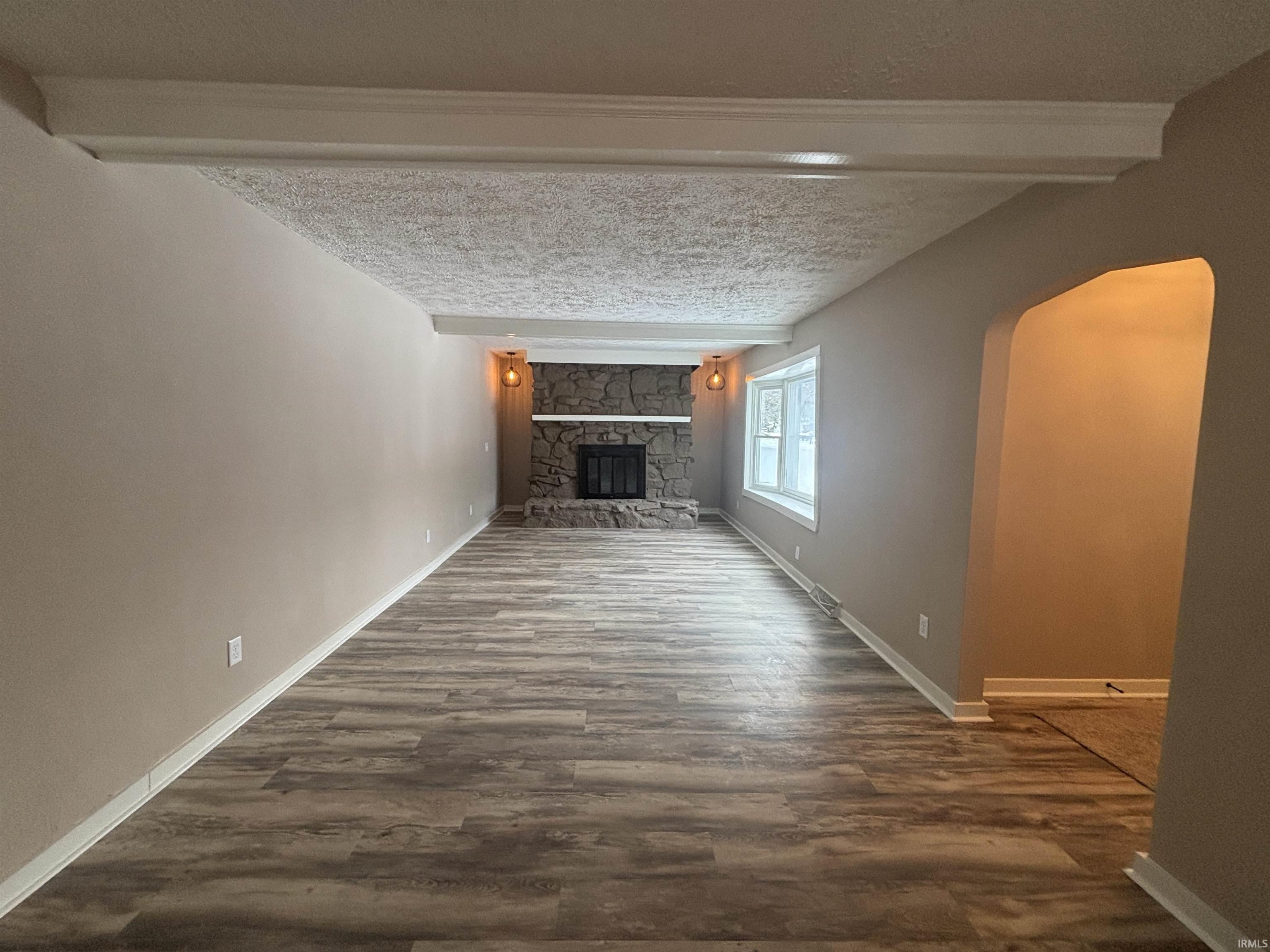 Unfurnished living room with arched walkways, a textured ceiling, dark wood-style floors, and a fireplace