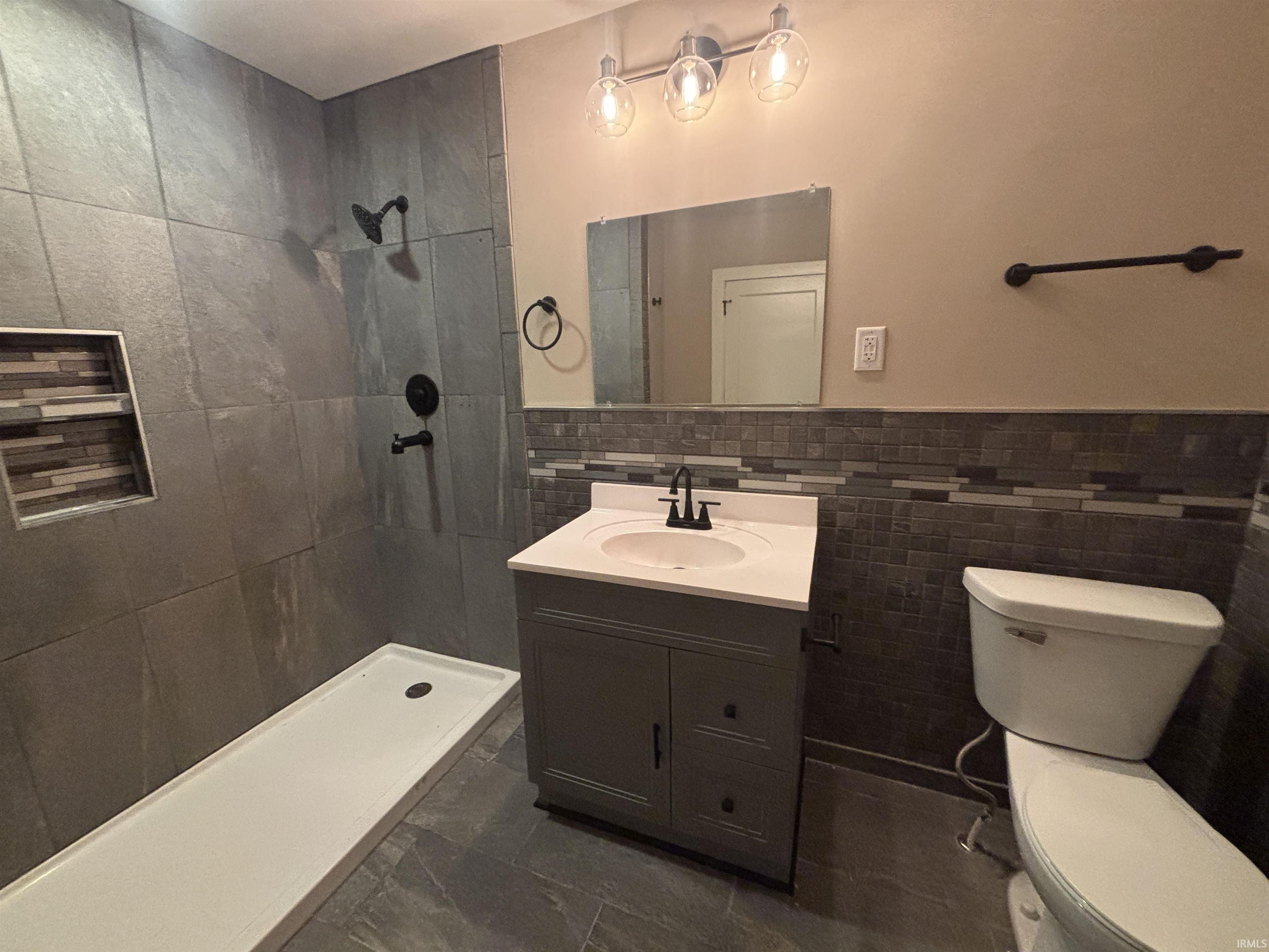 Full bathroom featuring a tile shower, vanity, tile walls, and a wainscoted wall