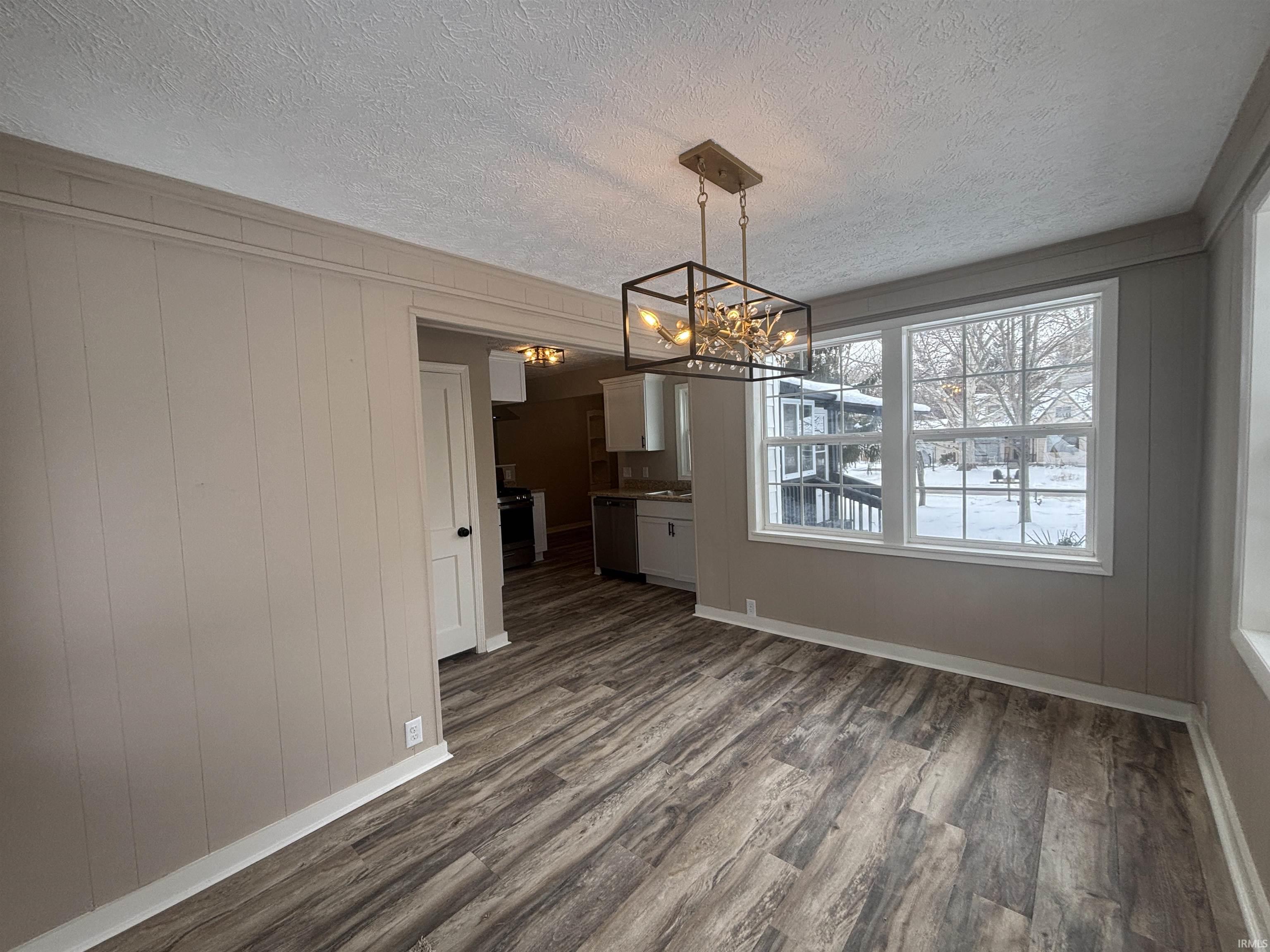 Unfurnished dining area featuring hanging lights, wooden walls, dark wood-type flooring, and a textured ceiling