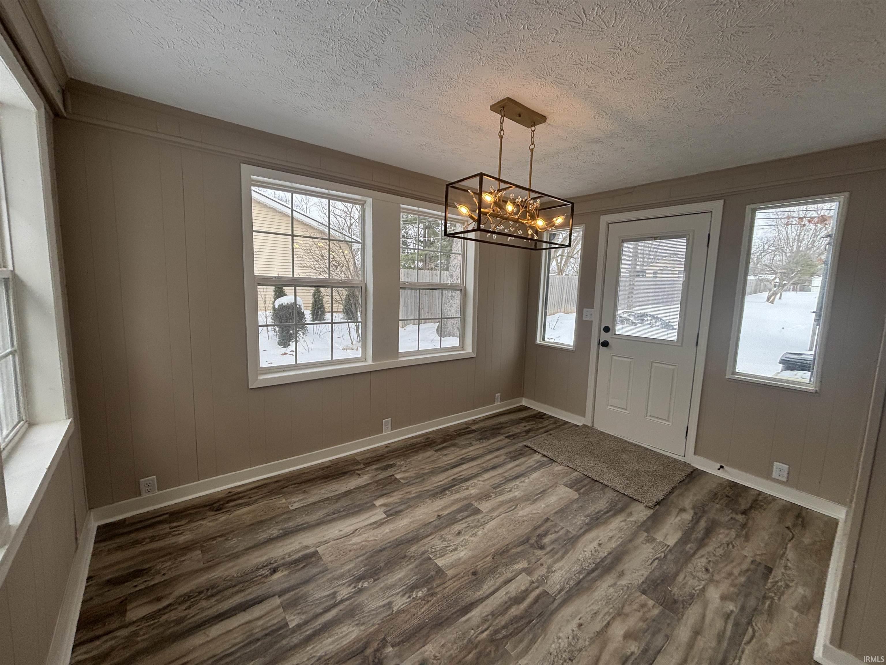 Unfurnished dining area featuring wooden walls, a chandelier, a textured ceiling, and wood finished floors