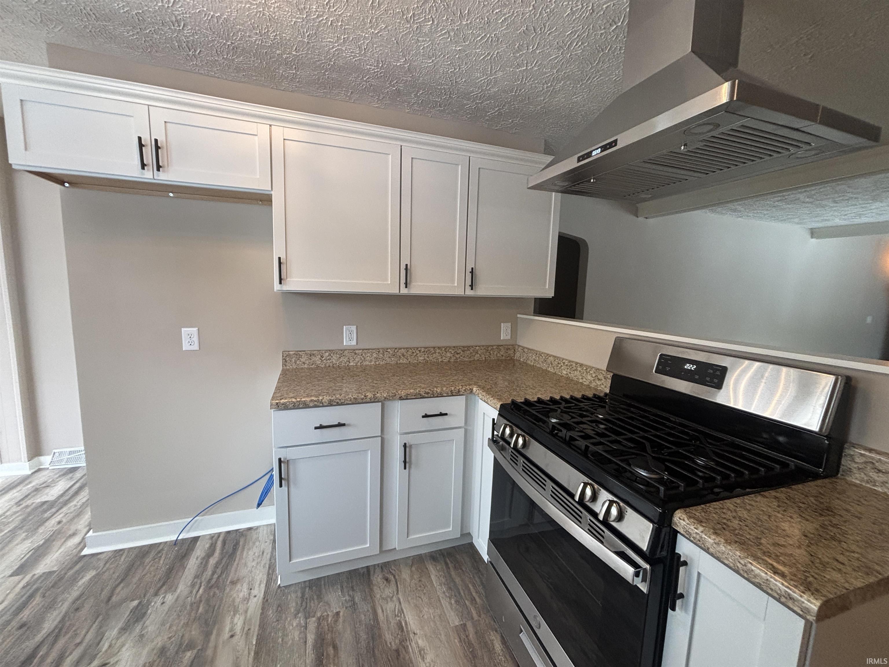 Kitchen featuring stainless steel range with gas stovetop, a textured ceiling, white cabinets, dark wood-type flooring, and dark stone counters