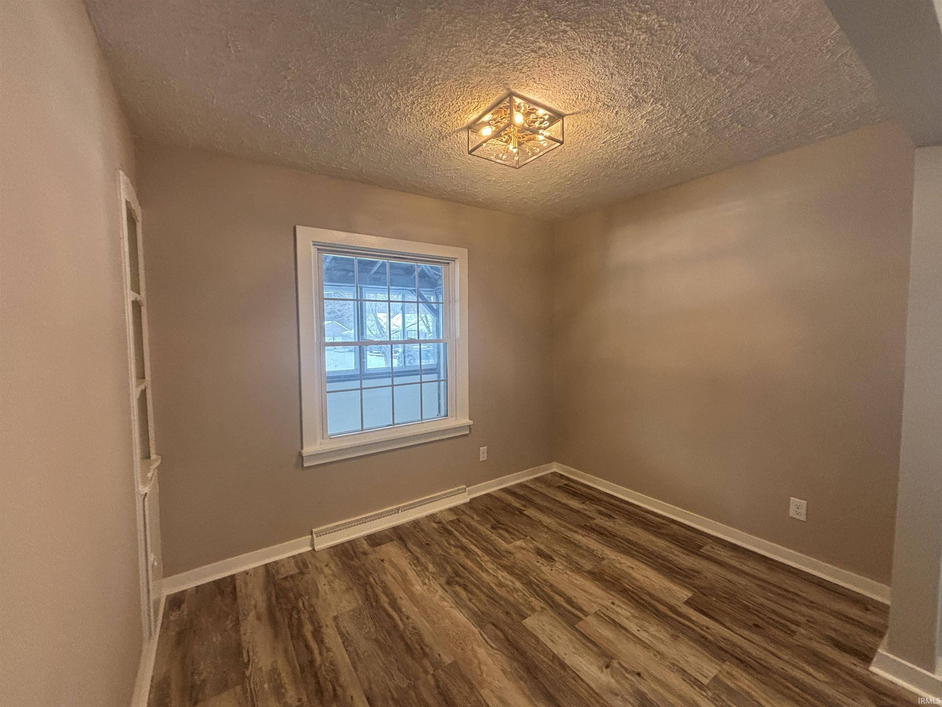 Unfurnished room featuring dark wood-type flooring and a textured ceiling