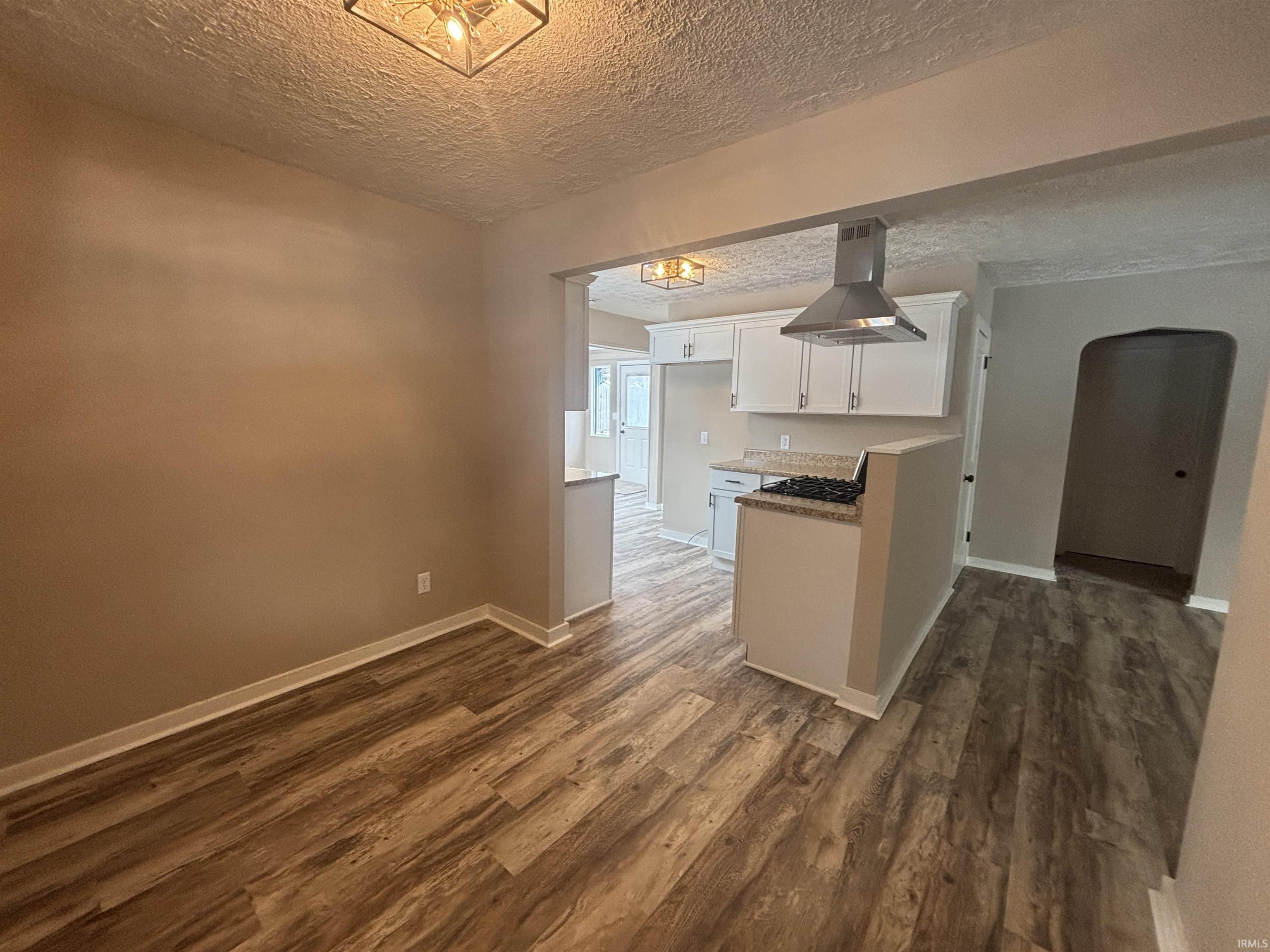 Kitchen with arched walkways, white cabinets, a textured ceiling, island range hood, and dark wood-style flooring