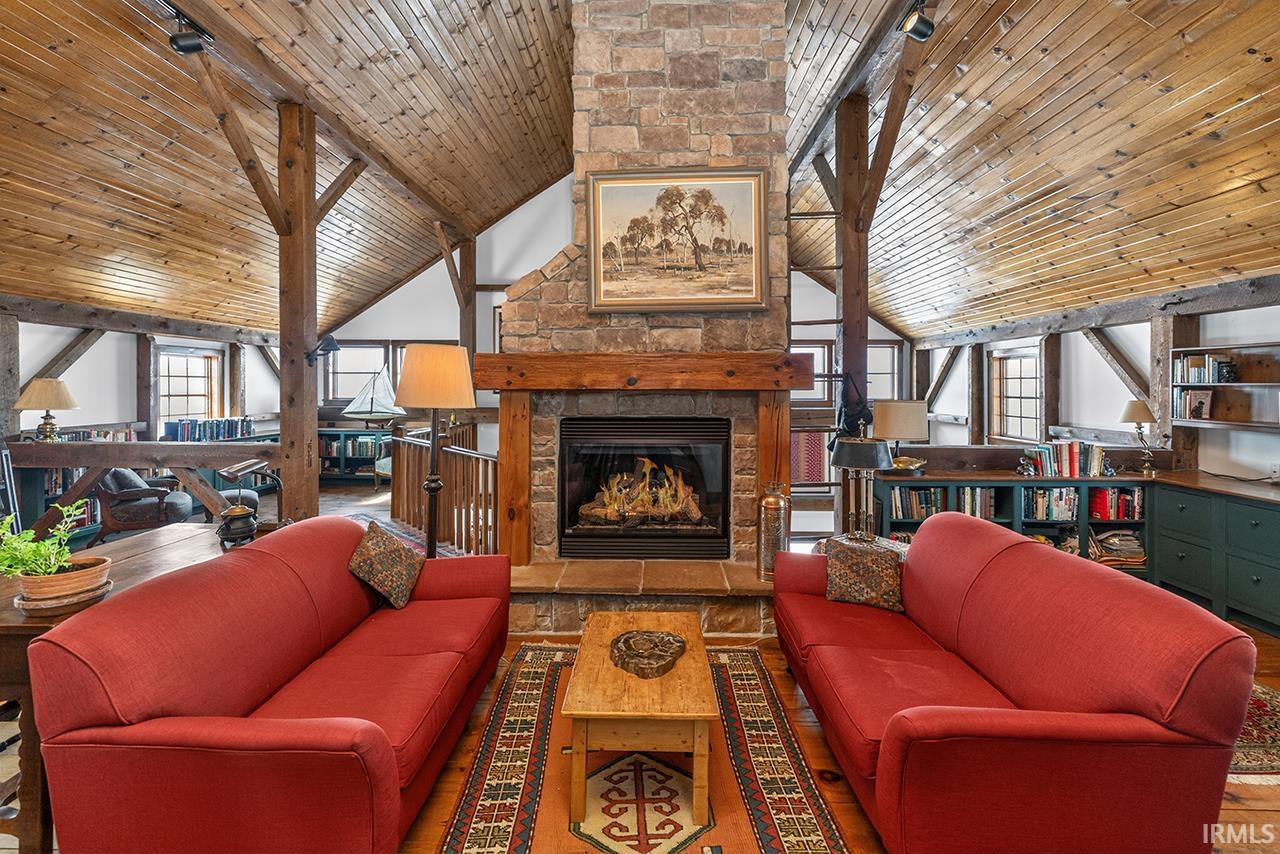 Living room with a stone fireplace, a vaulted wooden ceiling, and wood finished floors