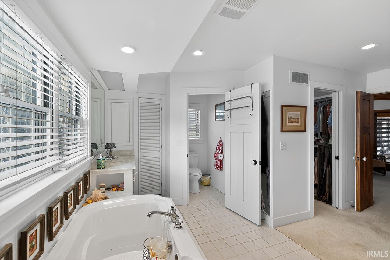 Bathroom with a garden tub, light carpet, light tile patterned flooring, recessed lighting, and a walk in closet