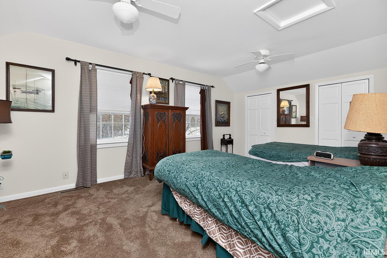 Carpeted bedroom featuring vaulted ceiling, two closets, and ceiling fan