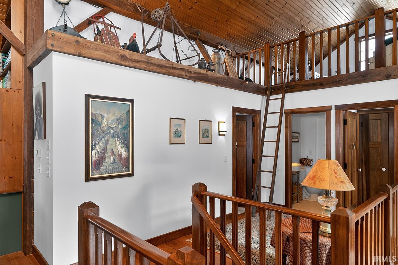 Hall with an upstairs landing, wood finished floors, and a vaulted wooden ceiling