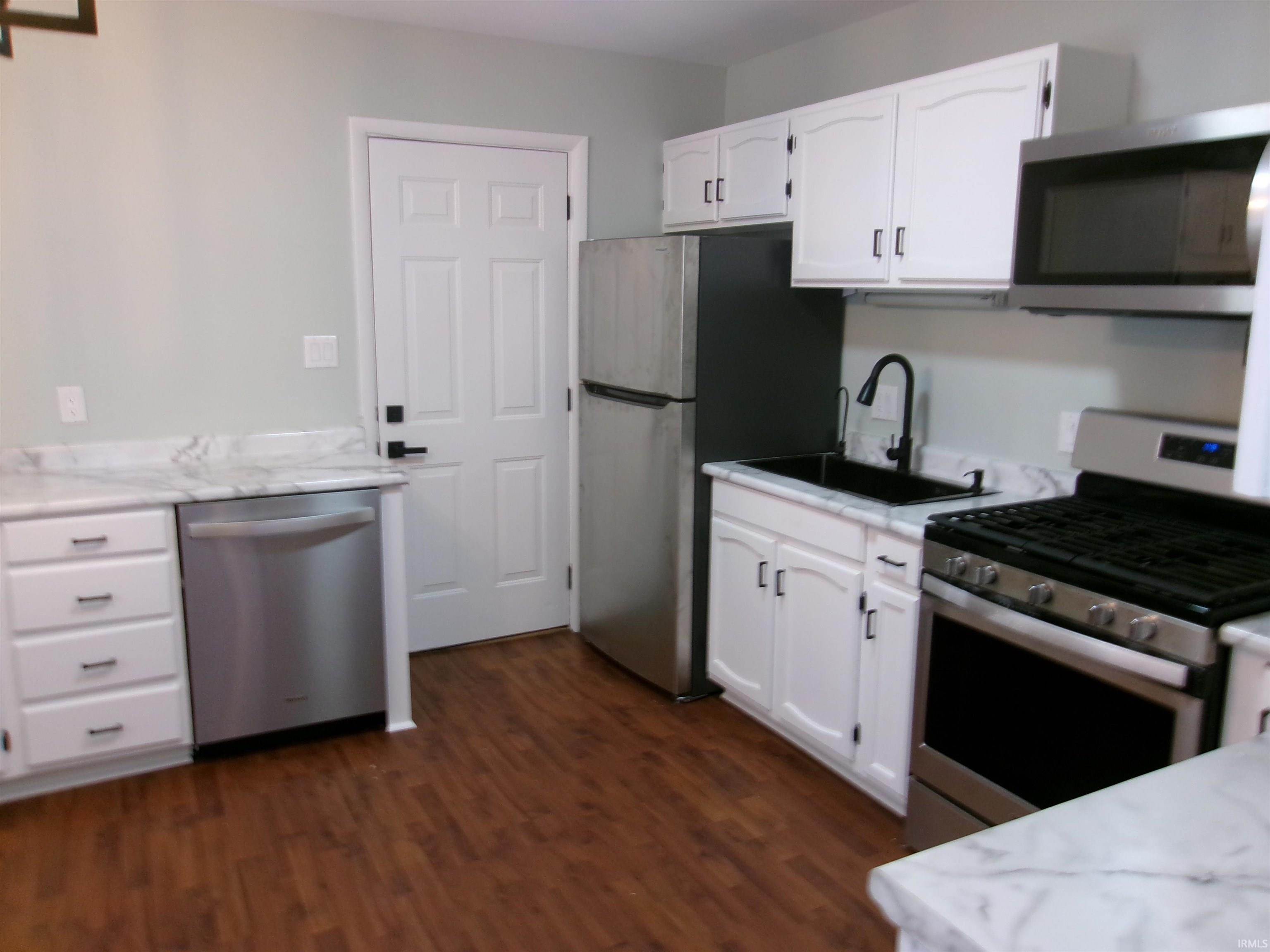 Kitchen with stainless steel appliances, white cabinets, dark wood-style flooring, and light stone countertops