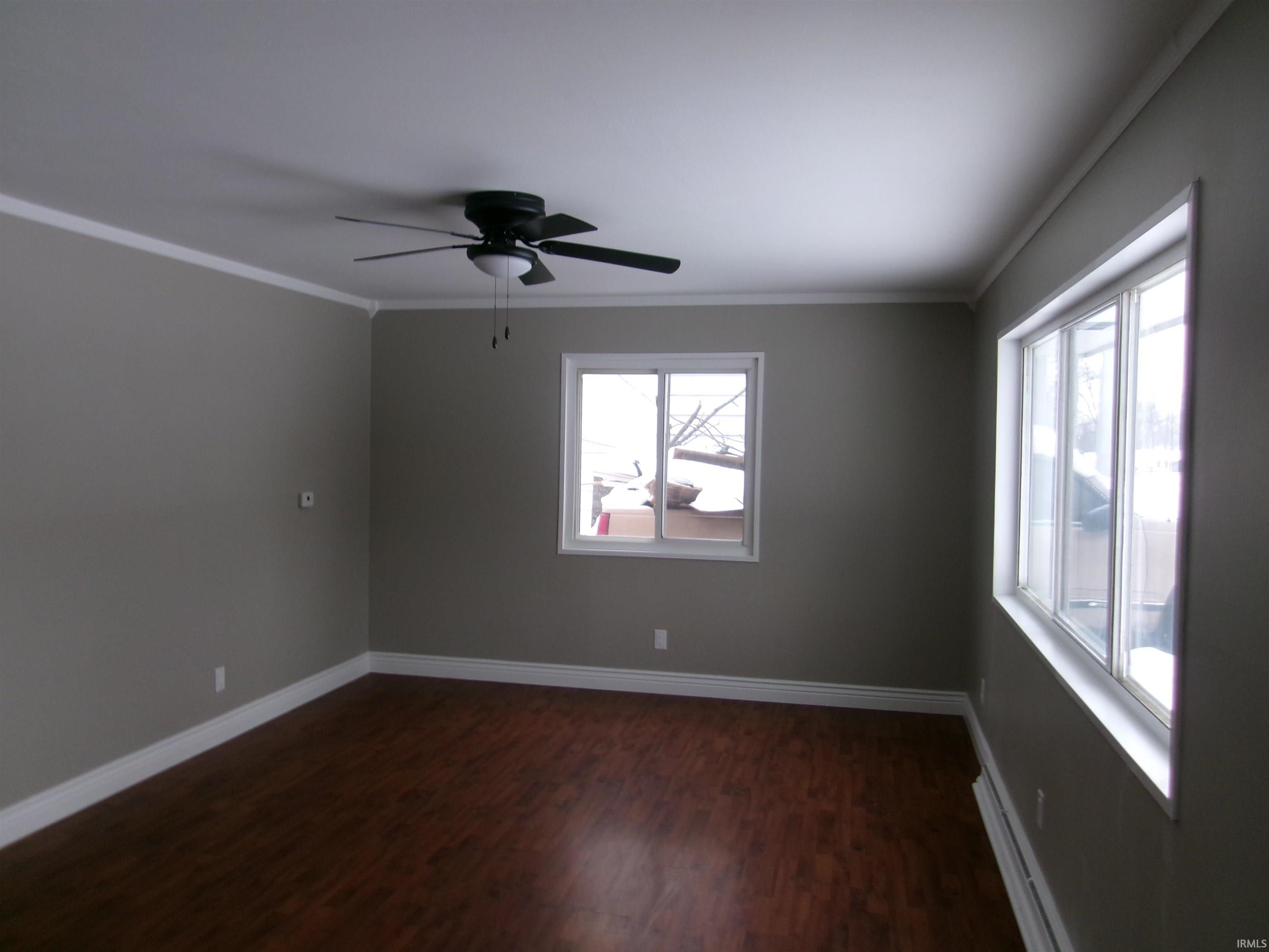 Spare room featuring a baseboard heating unit, dark wood-style flooring, ceiling fan, and ornamental molding