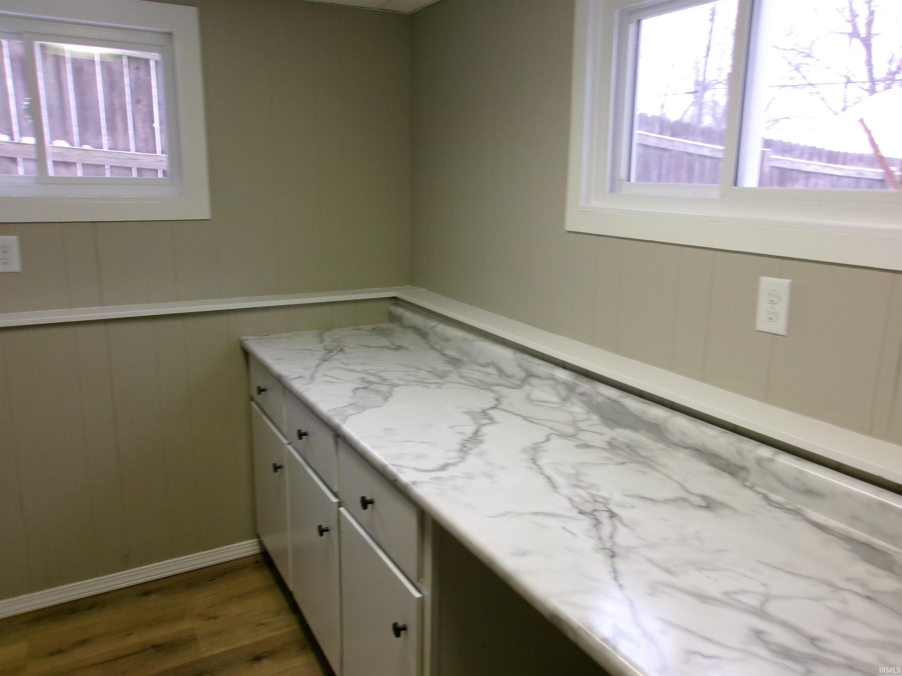 Interior space featuring white cabinets, dark wood-style flooring, wood walls, light stone countertops, and healthy amount of natural light