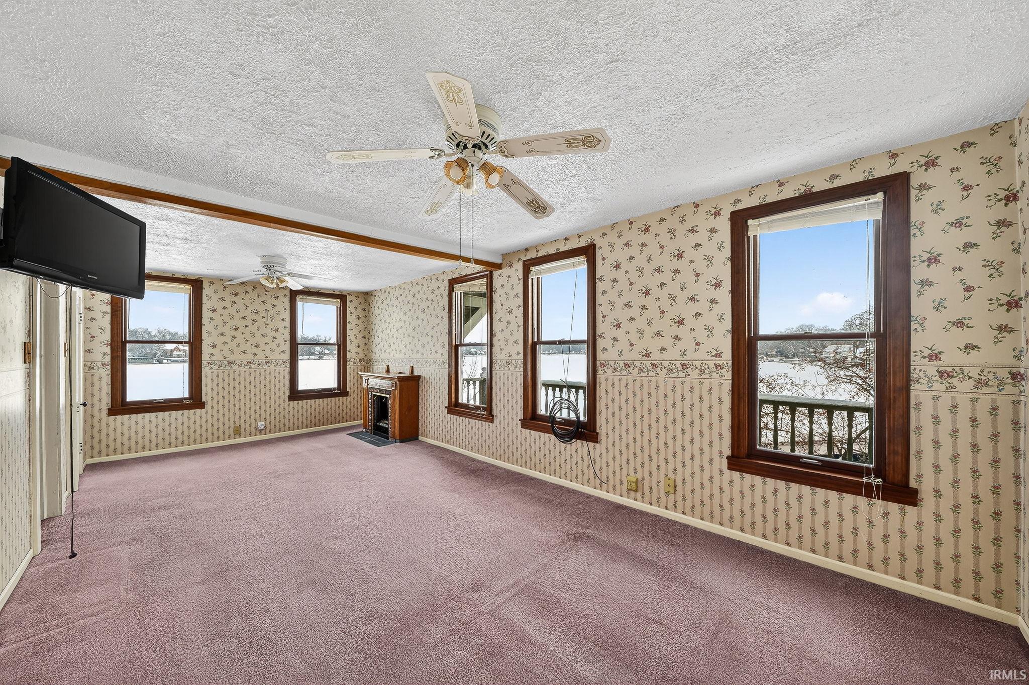 Unfurnished living room with a textured ceiling, wallpapered walls, carpet flooring, a ceiling fan, and a fireplace with flush hearth