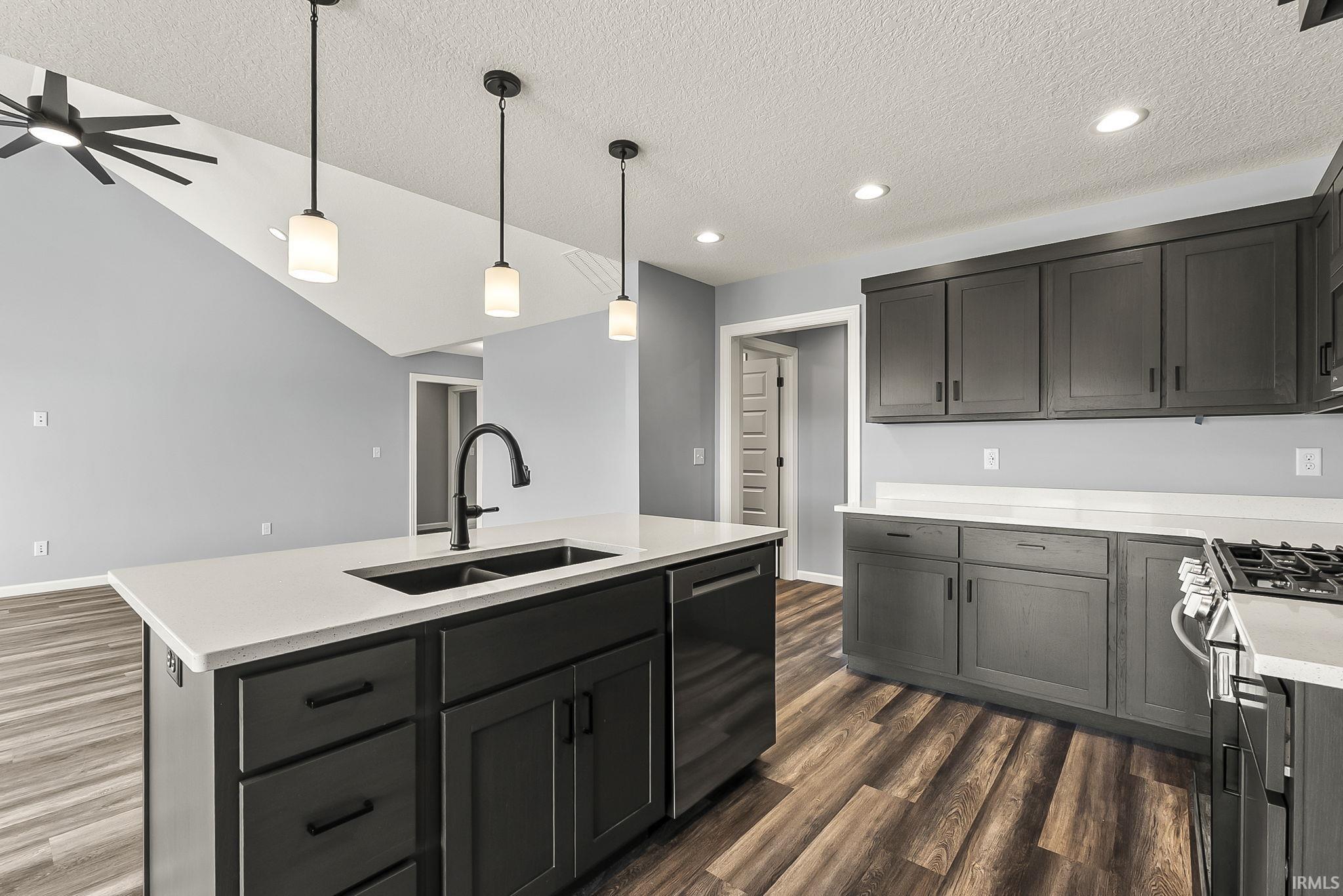 Kitchen featuring a textured ceiling, hanging light fixtures, a center island with sink, stainless steel appliances, and dark wood-style floors