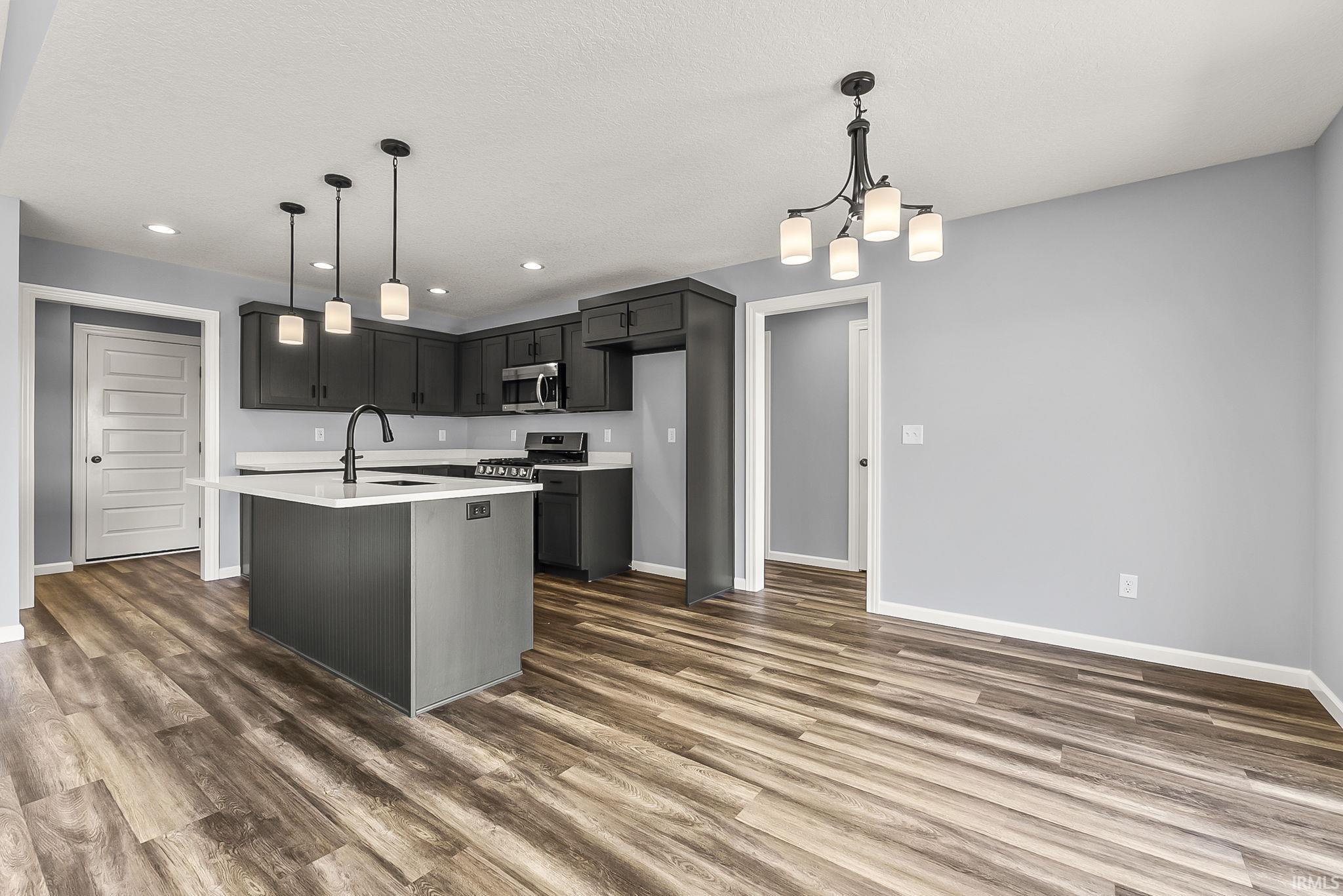 Kitchen featuring a kitchen island with sink, stainless steel appliances, a chandelier, dark wood-style flooring, and gray cabinets
