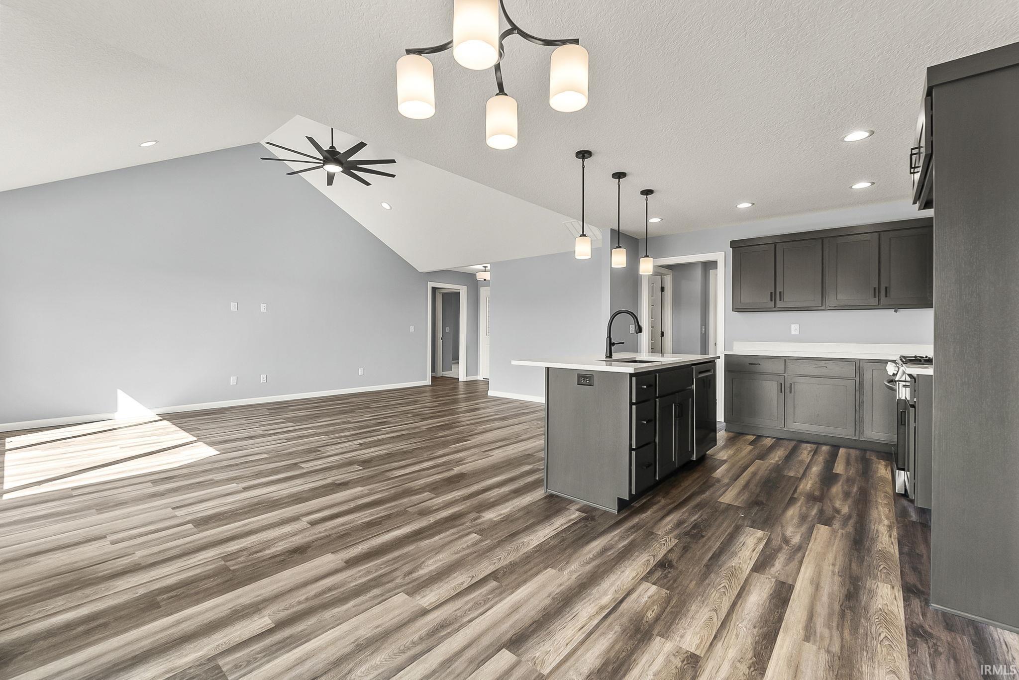 Kitchen featuring an island with sink, ceiling fan, pendant lighting, dark wood finished floors, and open floor plan