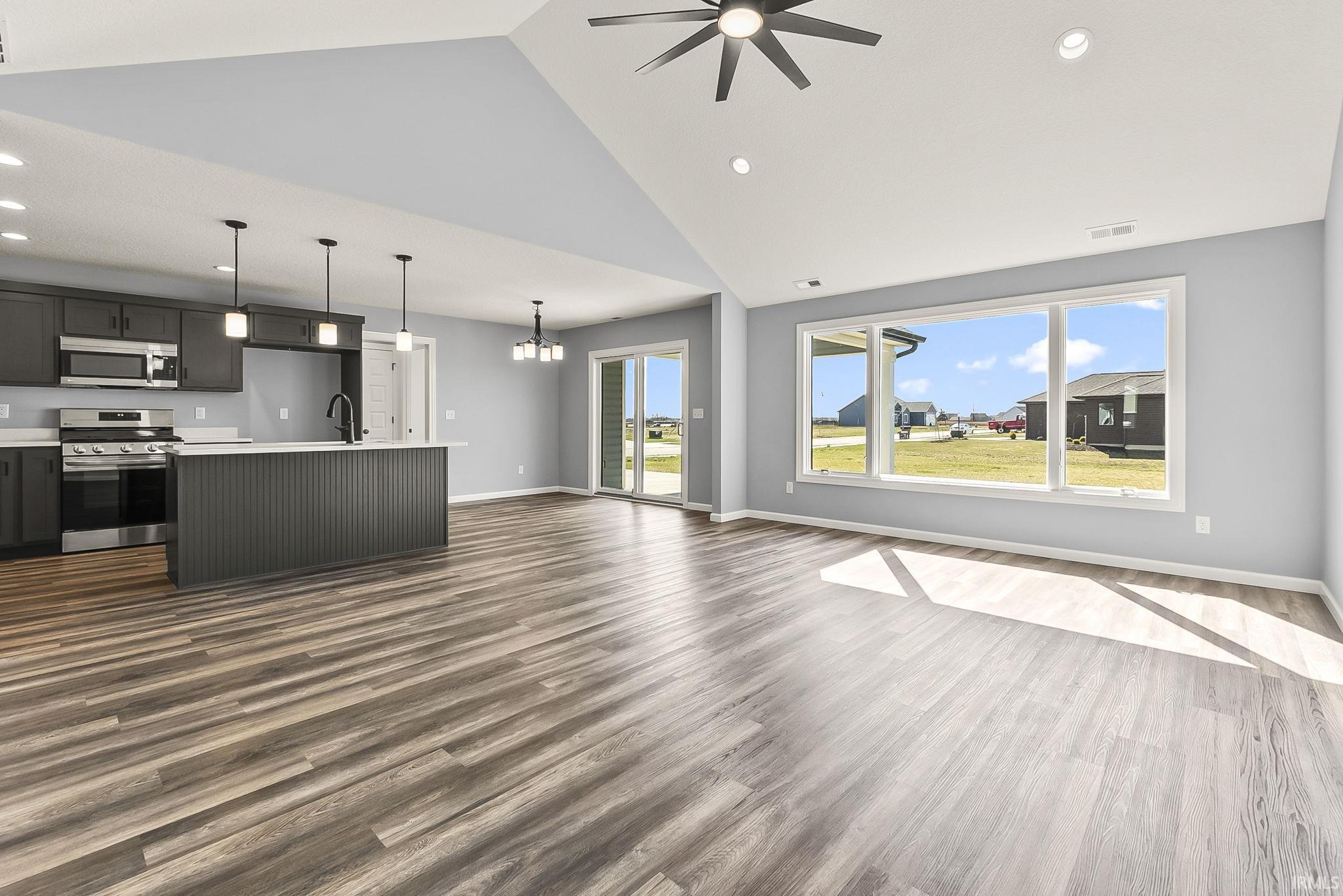 Unfurnished living room featuring ceiling fan, hanging lights, dark wood finished floors, and lofted ceiling