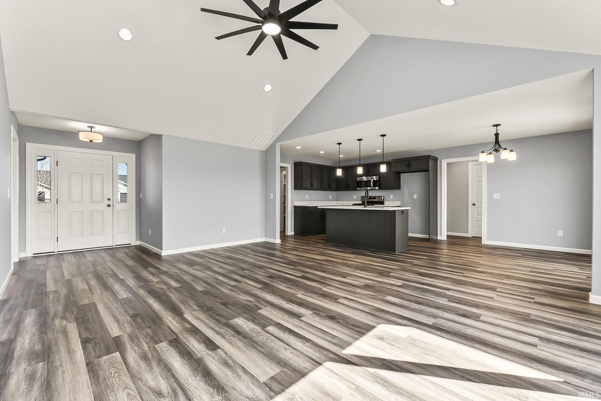 Unfurnished living room with a high ceiling, dark wood finished floors, ceiling fan, and suspended lighting