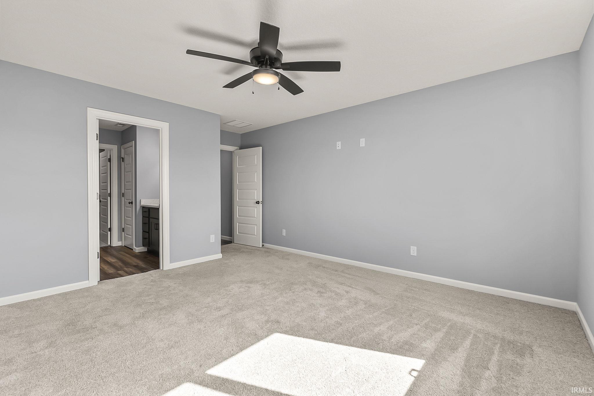 Unfurnished bedroom featuring light carpet, ensuite bathroom, and a ceiling fan