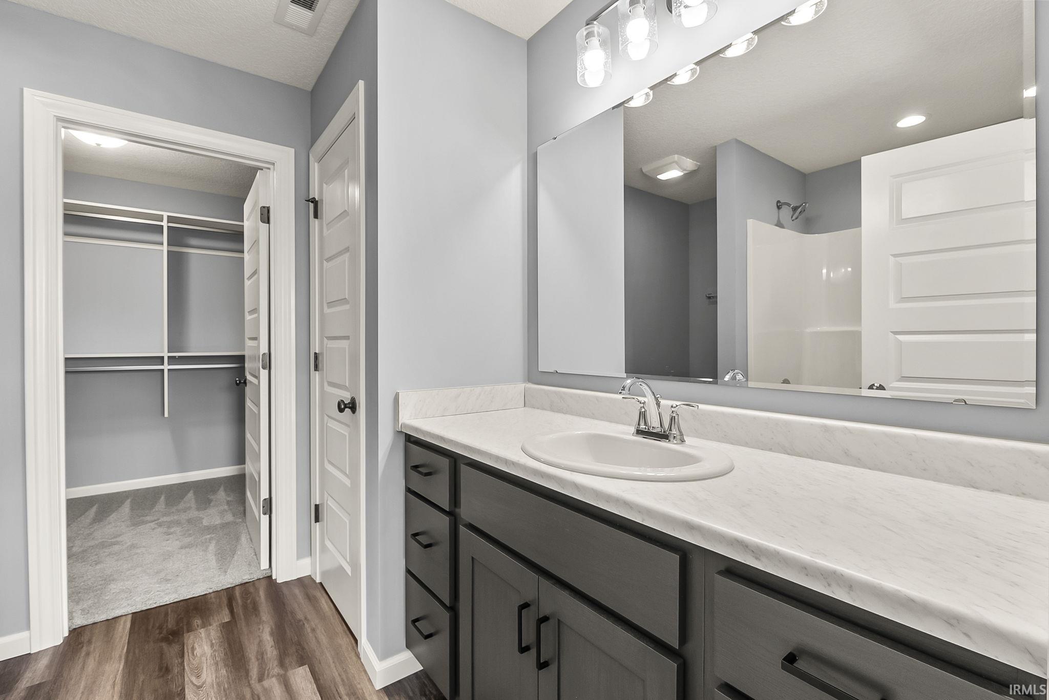 Full bath with vanity, a shower, dark wood-style floors, and a walk in closet