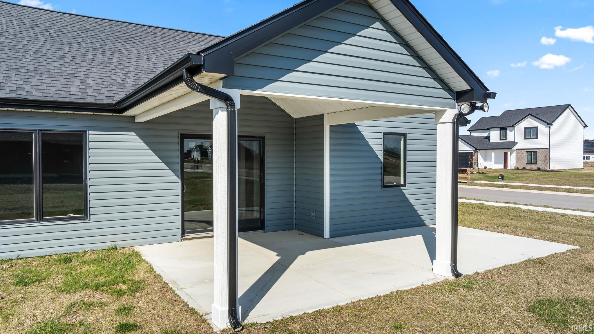 Entrance to property with a patio, a lawn, and a shingled roof