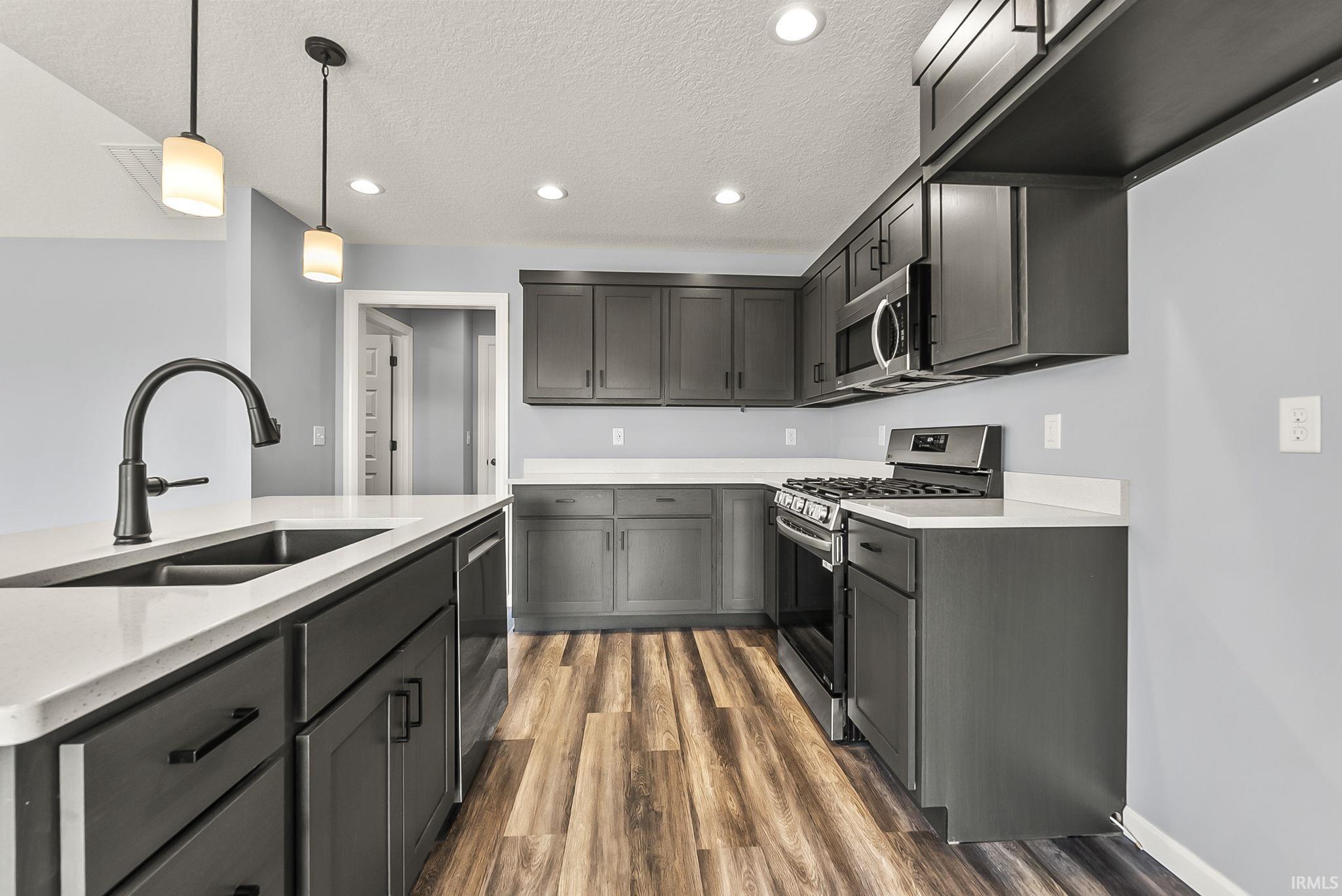 Kitchen featuring stainless steel appliances, decorative light fixtures, dark wood finished floors, a textured ceiling, and light stone counters