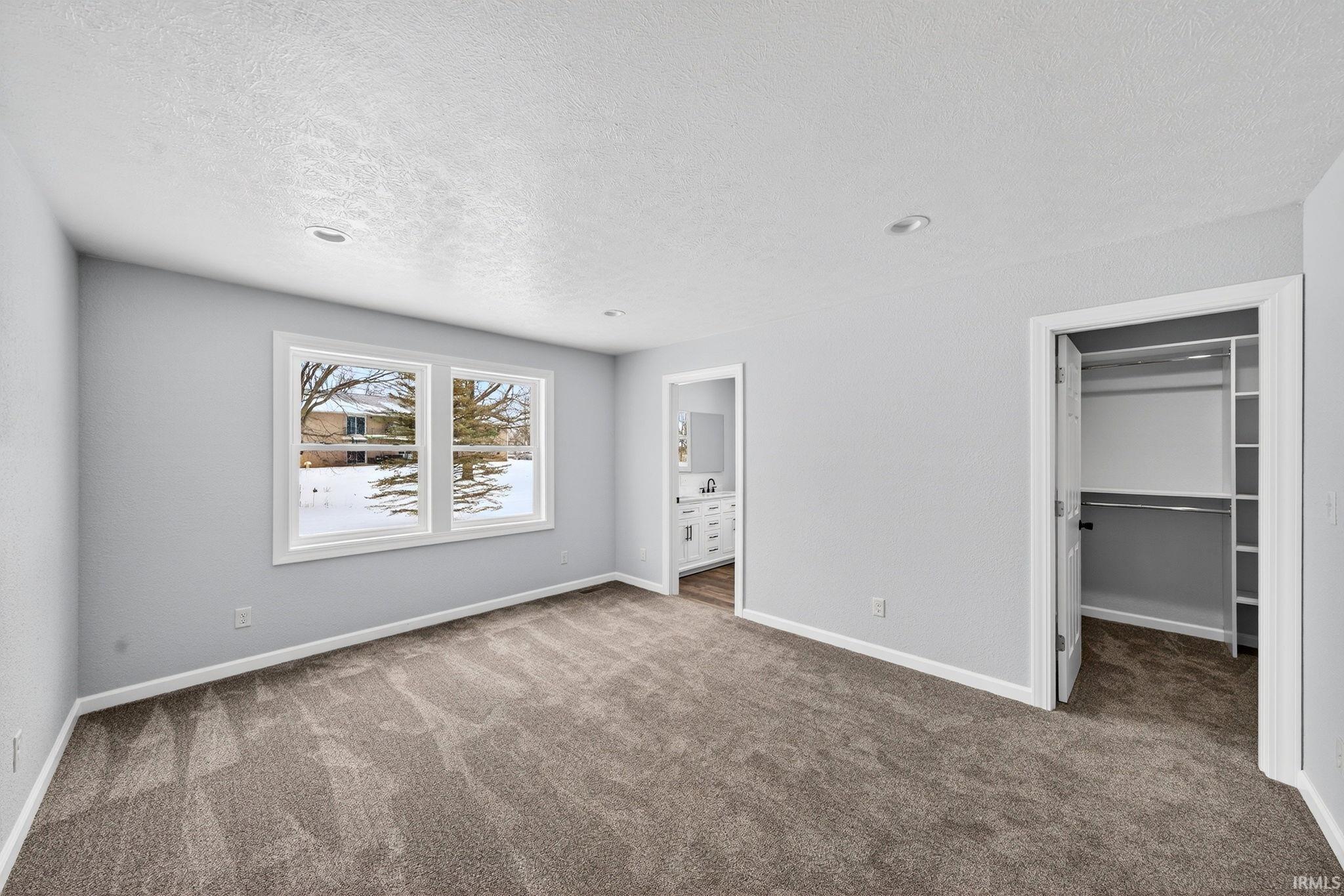 Unfurnished bedroom featuring a spacious closet, carpet, a textured ceiling, and ensuite bathroom