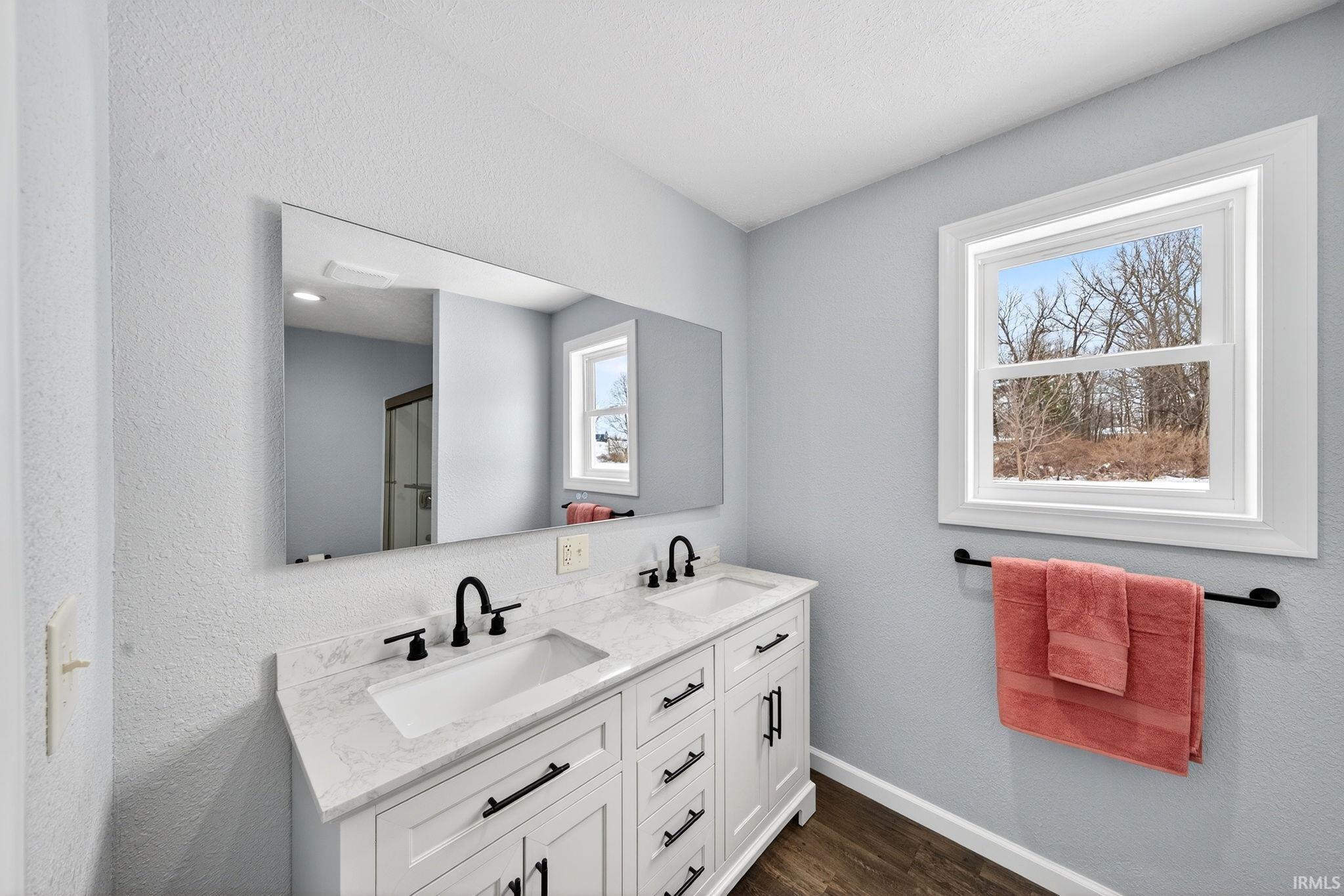 Bathroom featuring a textured wall, double vanity, and dark wood-style floors
