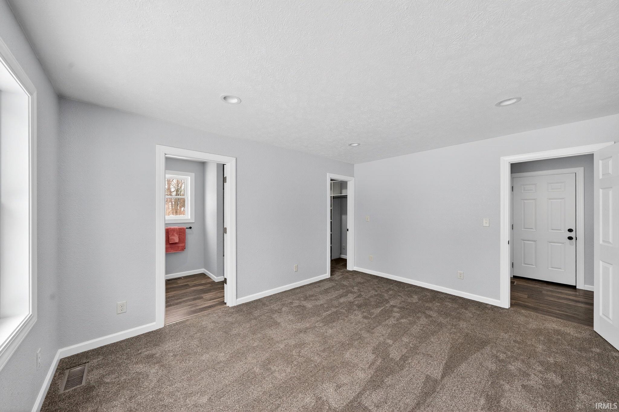 Unfurnished bedroom featuring a walk in closet, dark carpet, and a textured ceiling