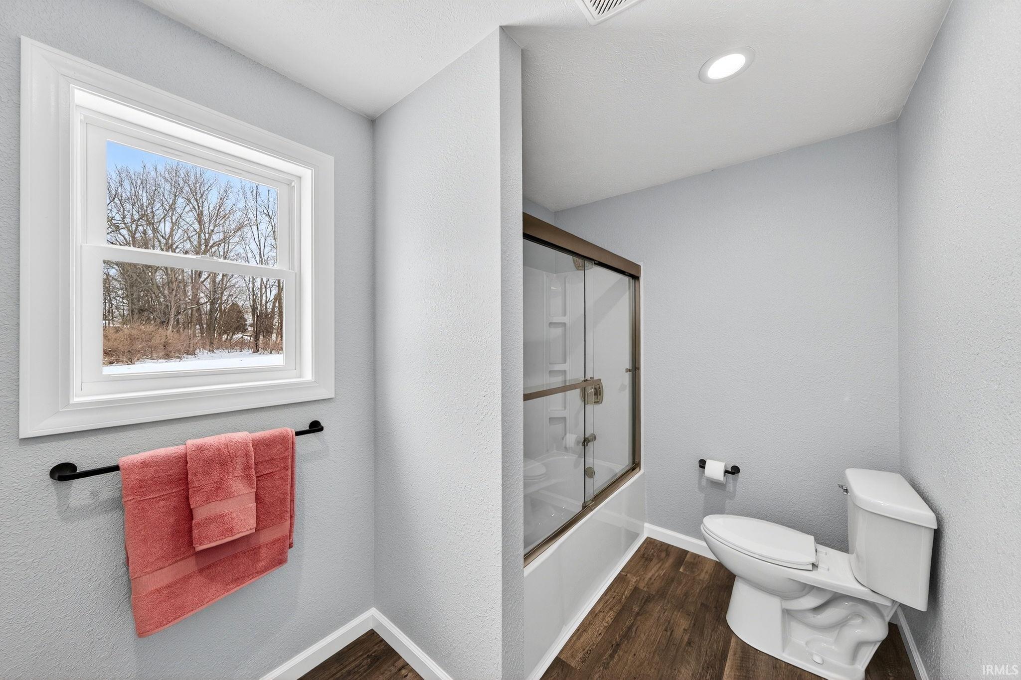 Full bathroom with shower / bath combination with glass door, dark wood-style flooring, and a textured wall