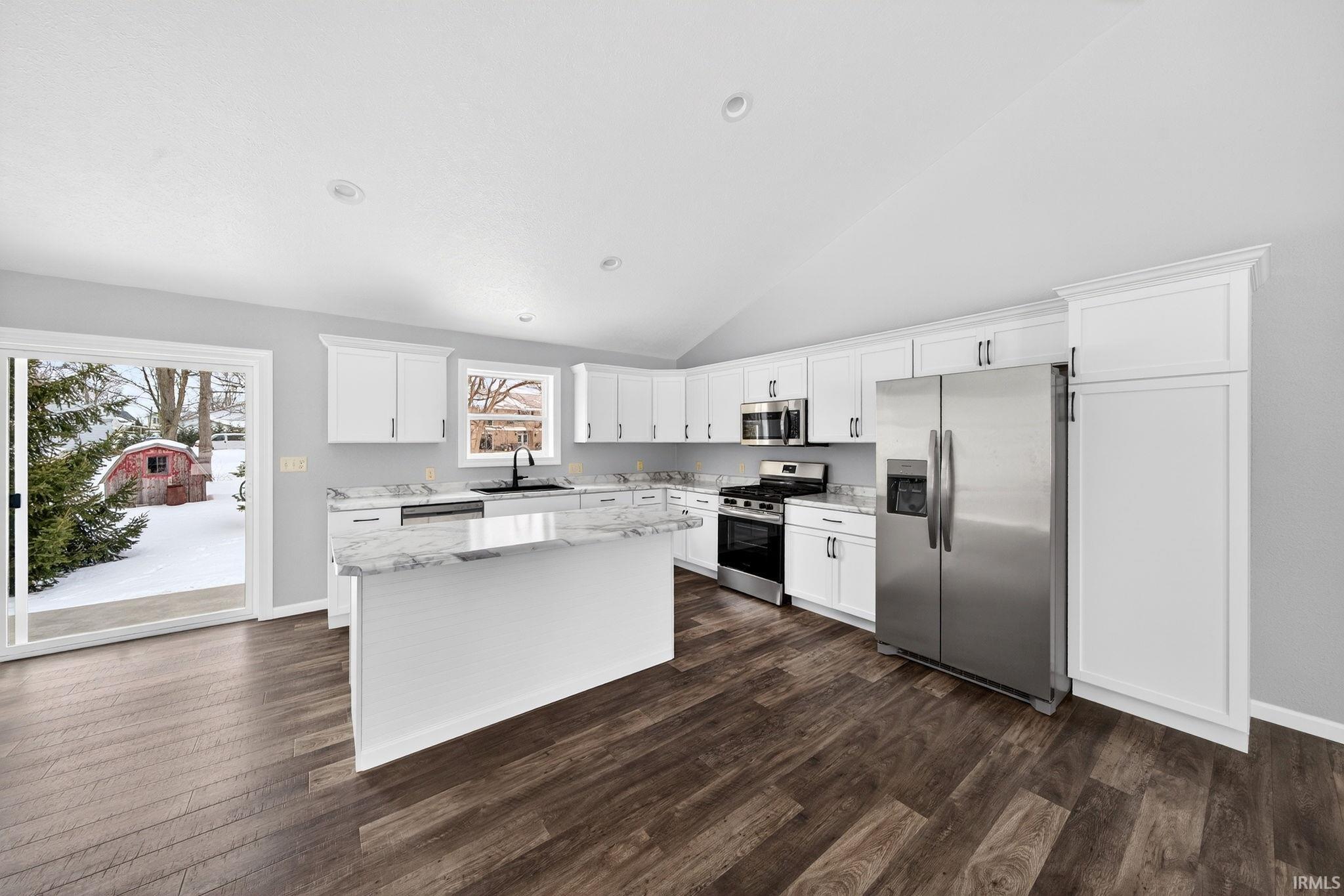 Kitchen featuring stainless steel appliances, white cabinets, light stone countertops, a kitchen island, and dark wood-style floors