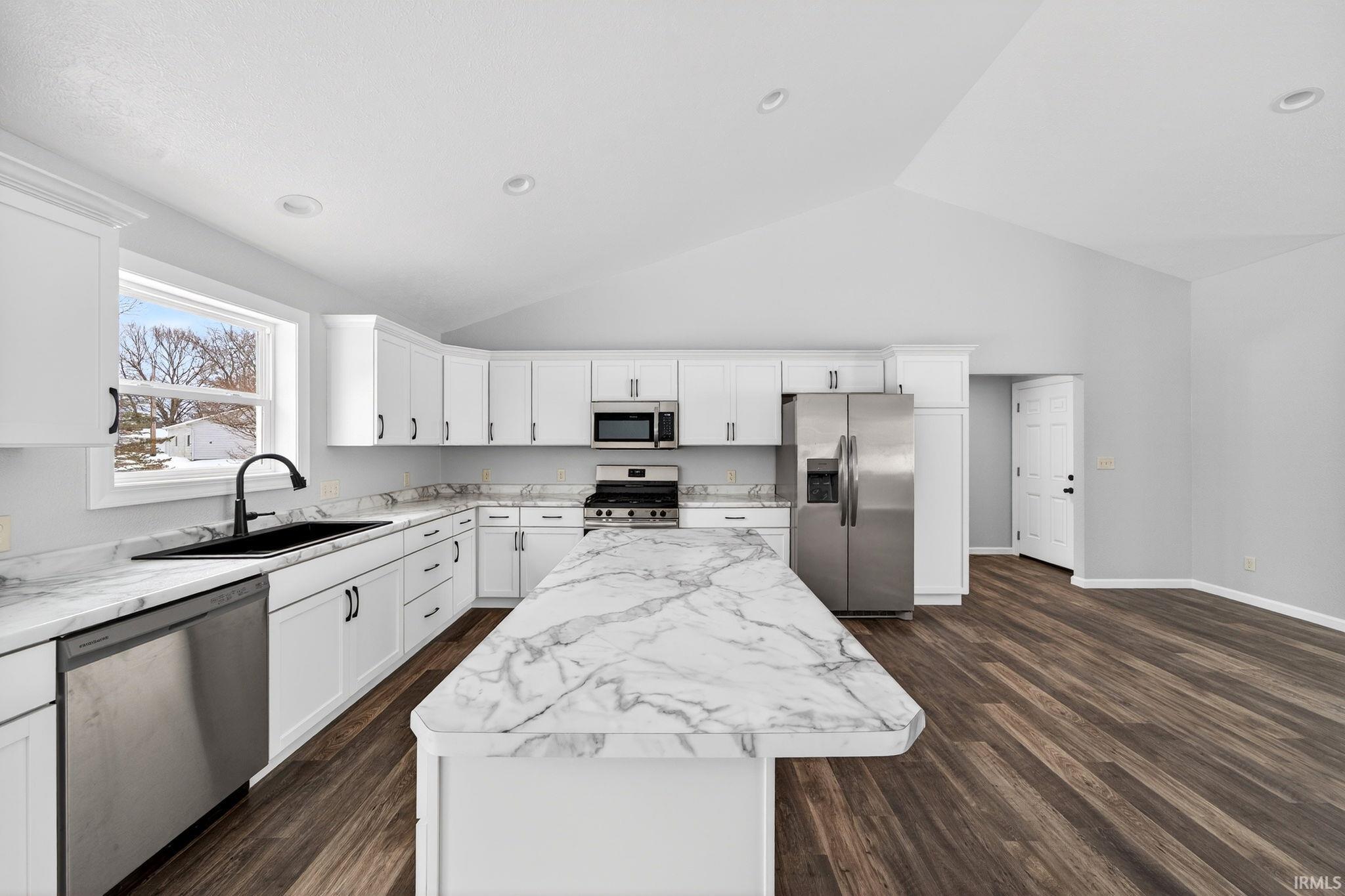 Kitchen with stainless steel appliances, white cabinetry, dark wood-style floors, a kitchen island, and lofted ceiling