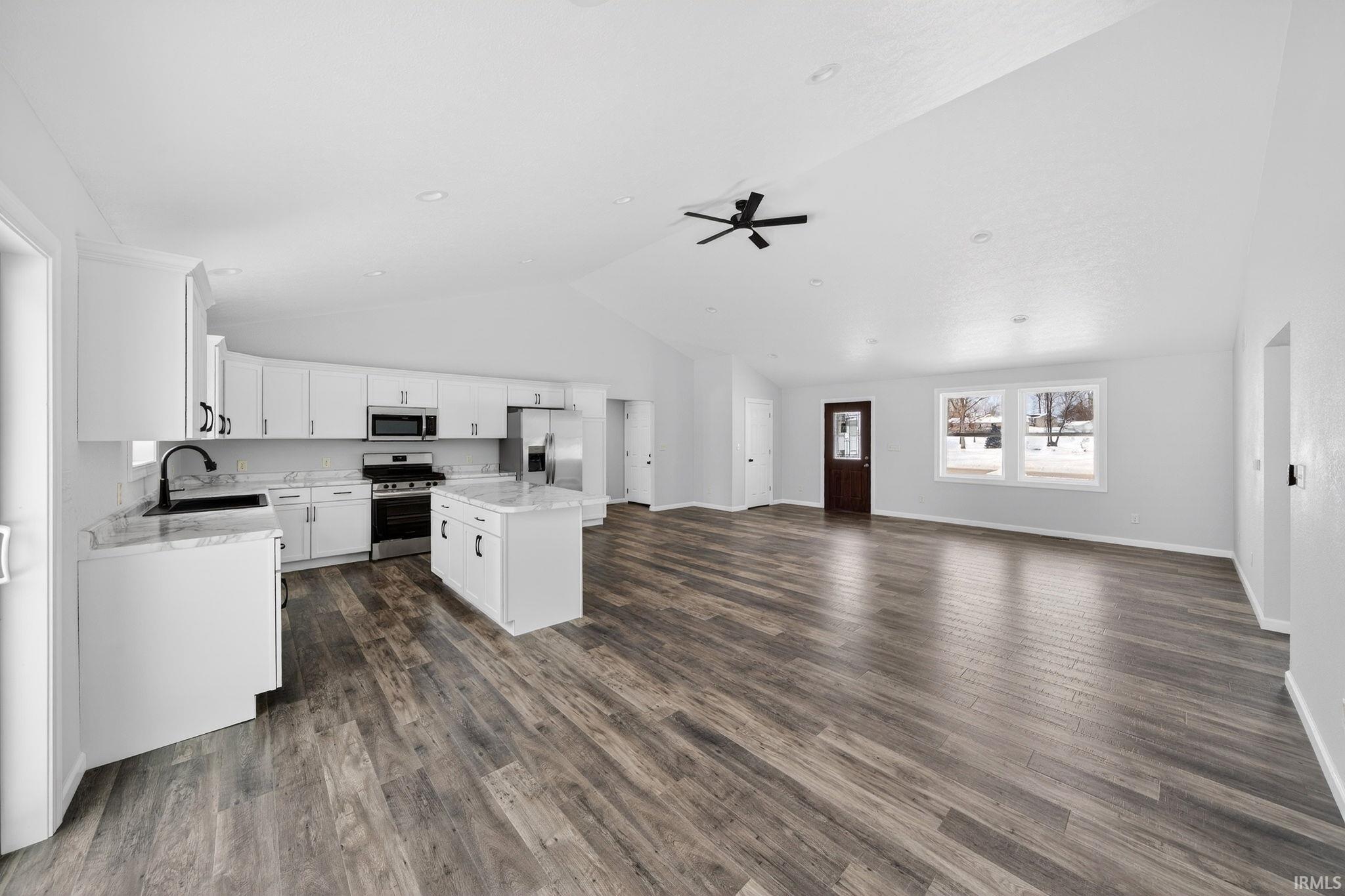 Kitchen featuring open floor plan, stainless steel appliances, white cabinetry, a center island, and lofted ceiling