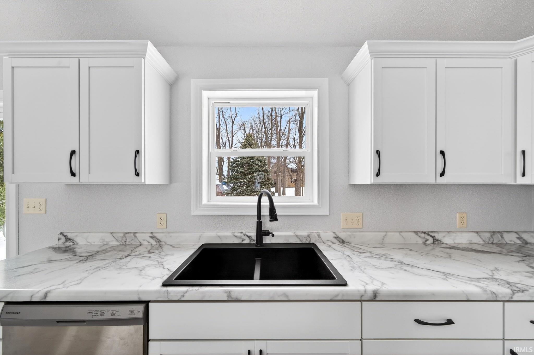 Kitchen featuring white cabinetry, stainless steel dishwasher, and light stone counters